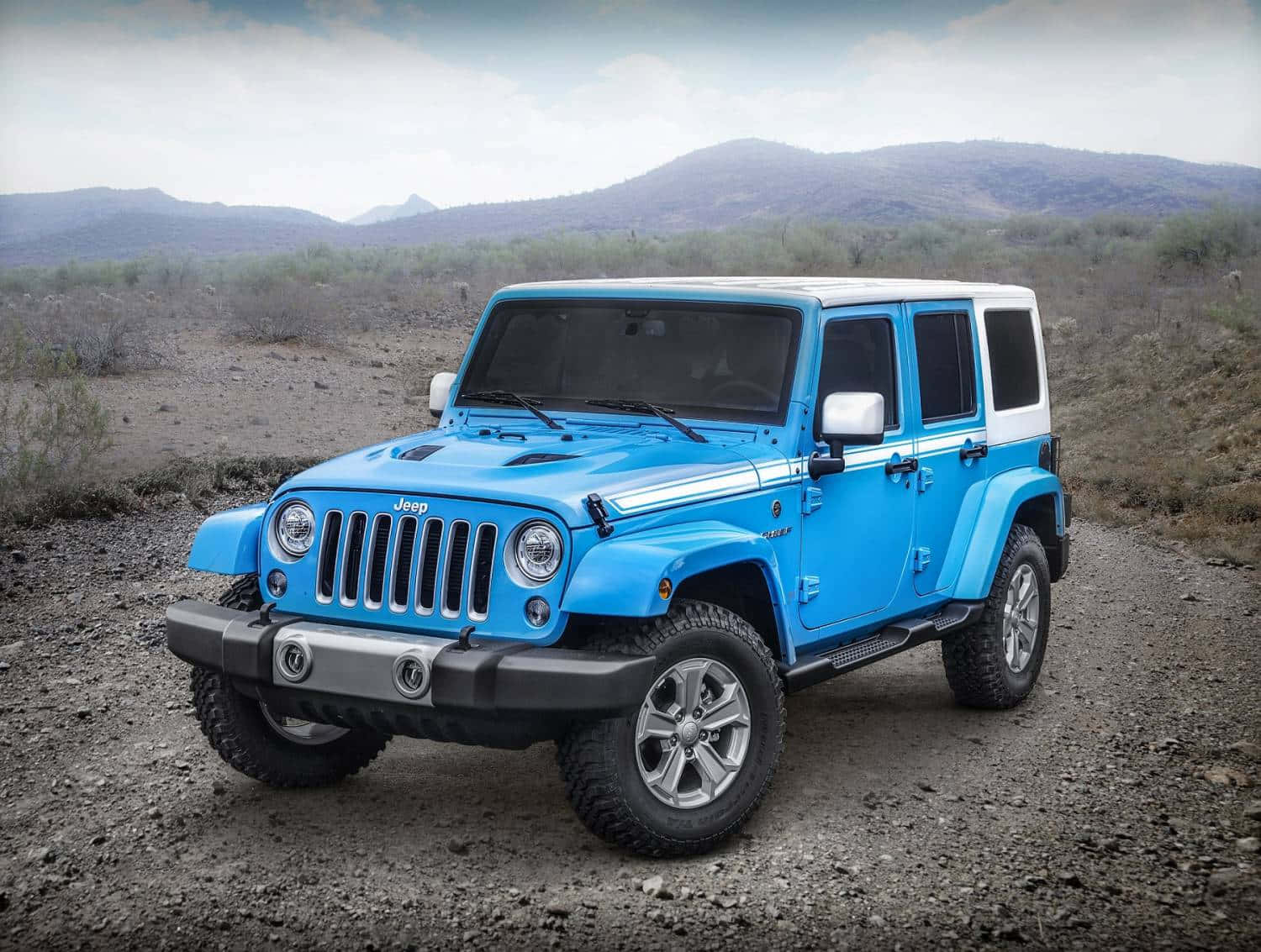 Jeep Wrangler 桌布 壁紙 — 一輛充滿活力的藍色Jeep Wrangler，白色車頂，停泊在乾燥山區沙漠景觀的碎石路上。