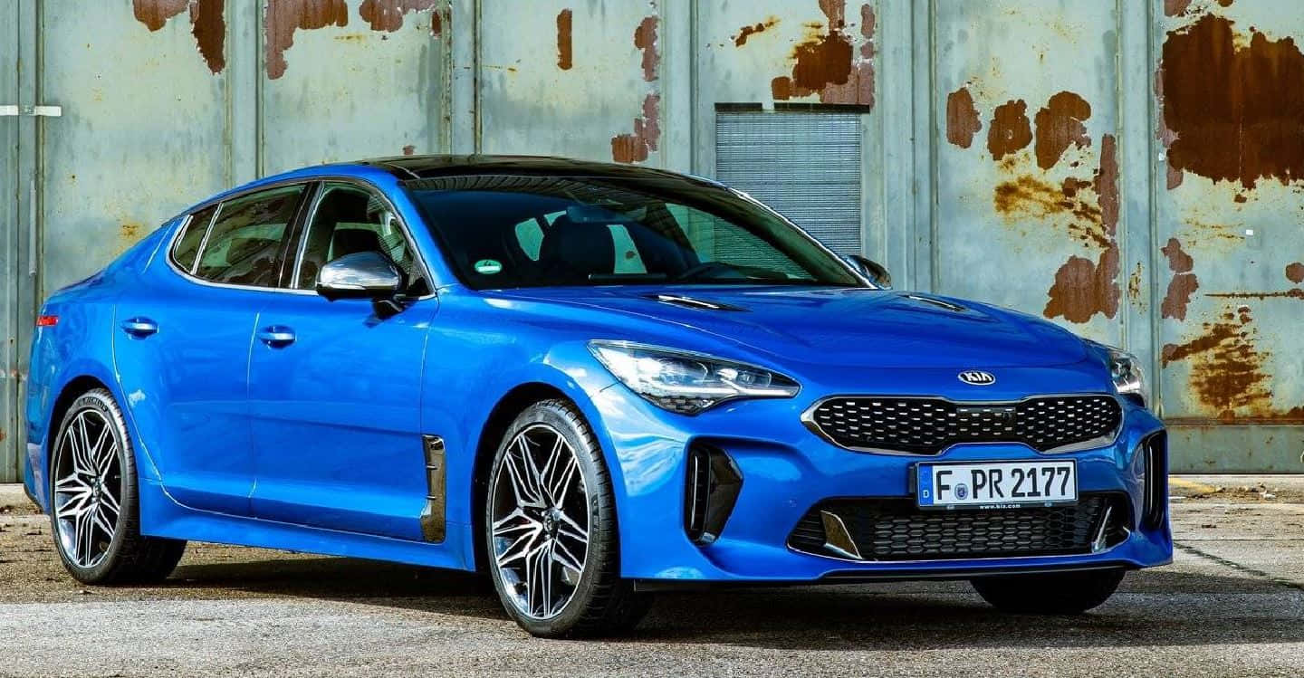 Kia Stinger 桌布 壁紙 — 一輛充滿活力的藍色Kia Stinger運動轎車停在風化的鏽蝕金屬牆前。