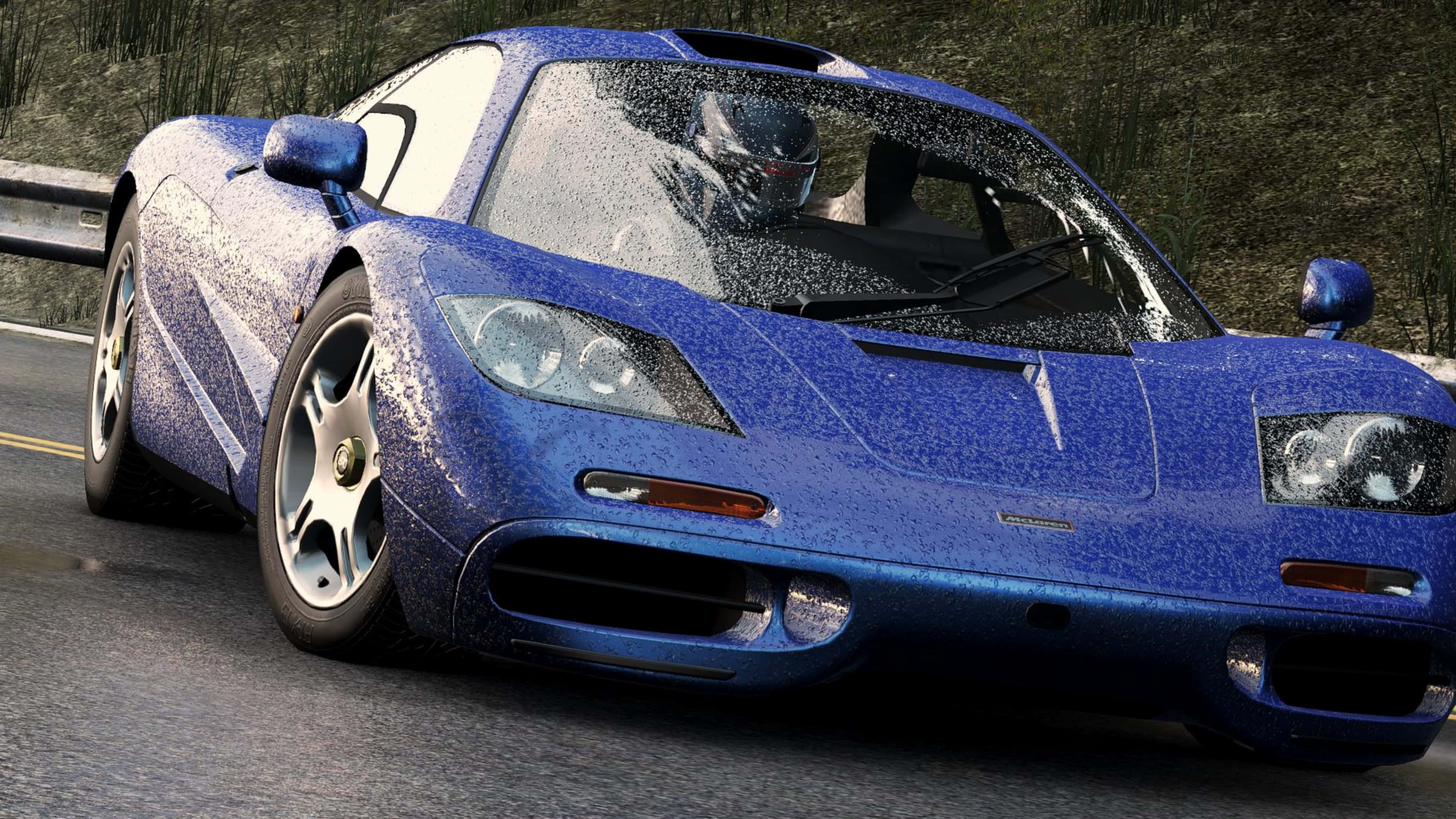 電玩遊戲 桌布 壁紙 — 一輛充滿活力的藍色McLaren F1跑車濺滿水珠，在潮濕的道路上疾馳，車內可見戴頭盔的司機。