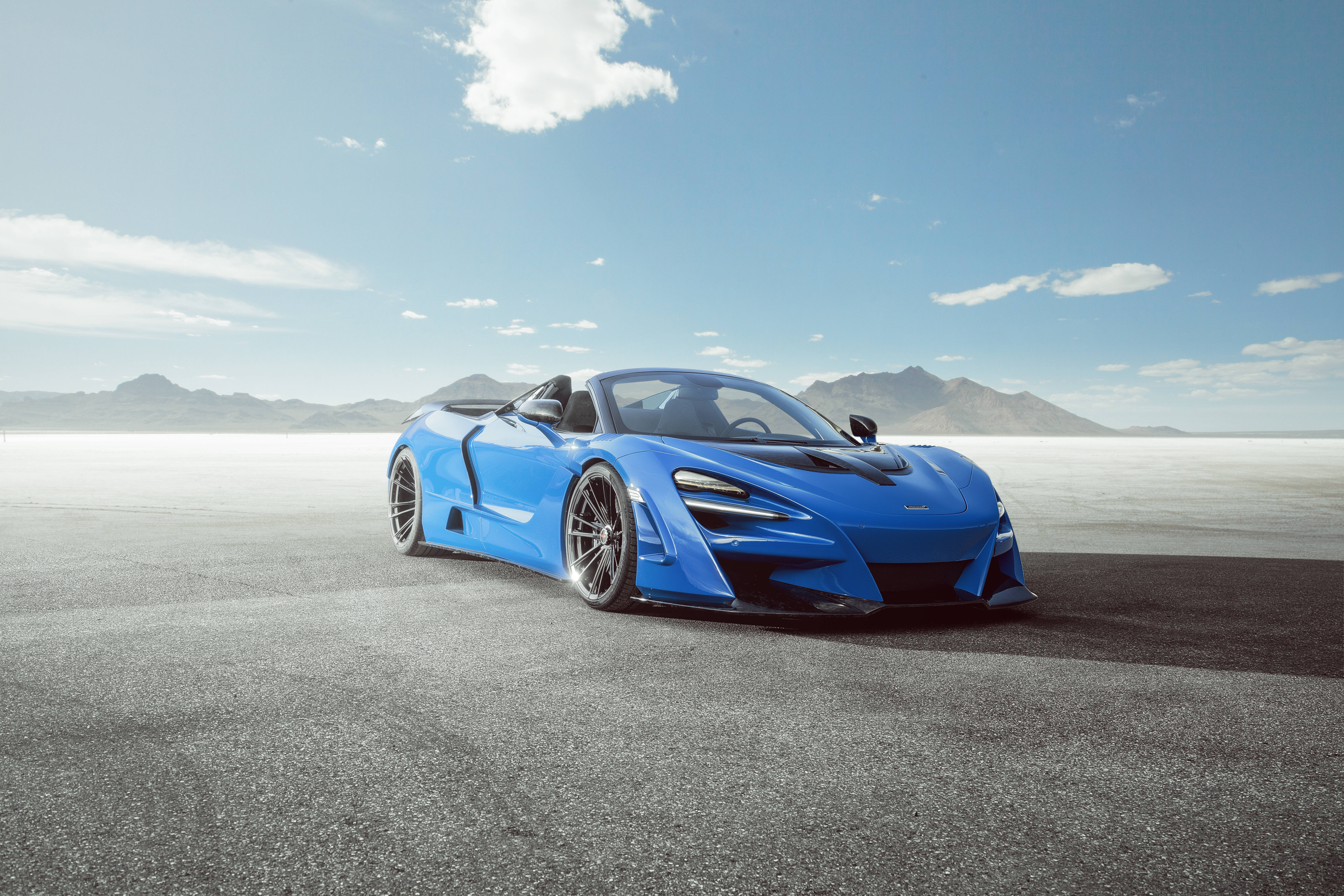 mclaren 720s 4K 桌布 壁紙 — 一輛充滿活力的藍色McLaren跑車停泊在廣闊的沙漠賽道上，天空清澈湛藍，遠處有山巒。
