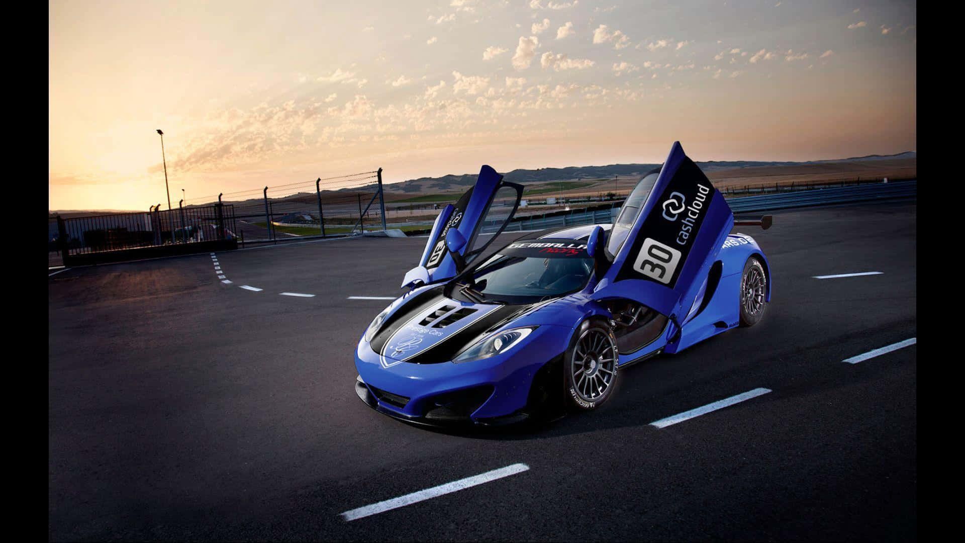高清 桌布 壁紙 — 一輛充滿活力的藍色McLaren跑車，蝴蝶門敞開，在日落時分停在賽道上。