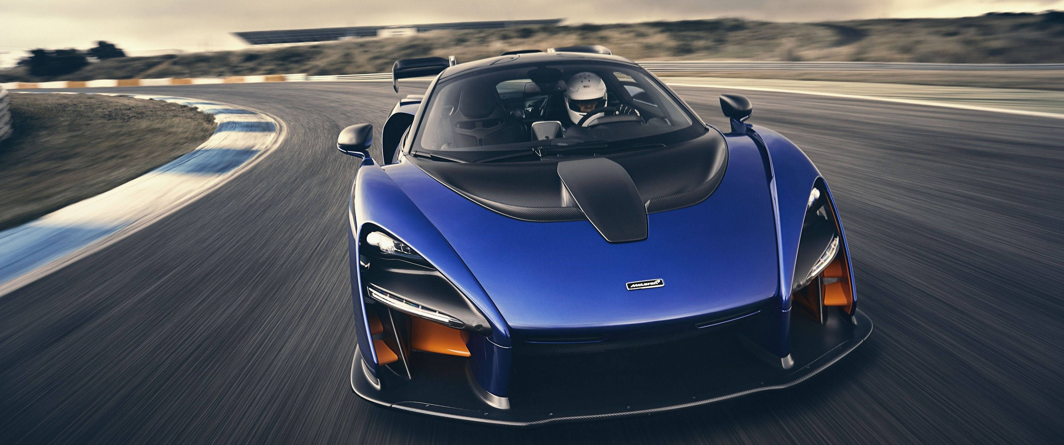 跑車 桌布 壁紙 — 一輛充滿活力的藍色McLaren Senna在賽道彎道上高速飛馳，動態模糊效果強調其高速。