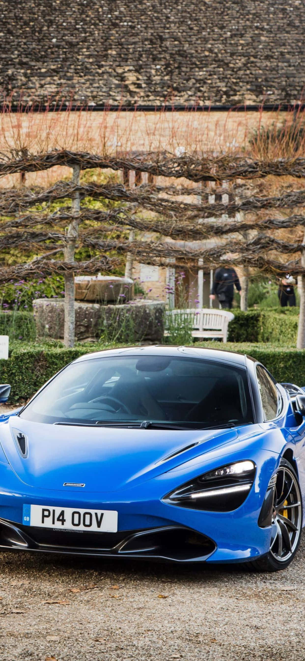 藍色 桌布 壁紙 — 一輛充滿活力的藍色McLaren跑車停在碎石路上，下方是鄉村風格的葡萄園涼棚，周圍有石牆和修剪整齊的樹籬。