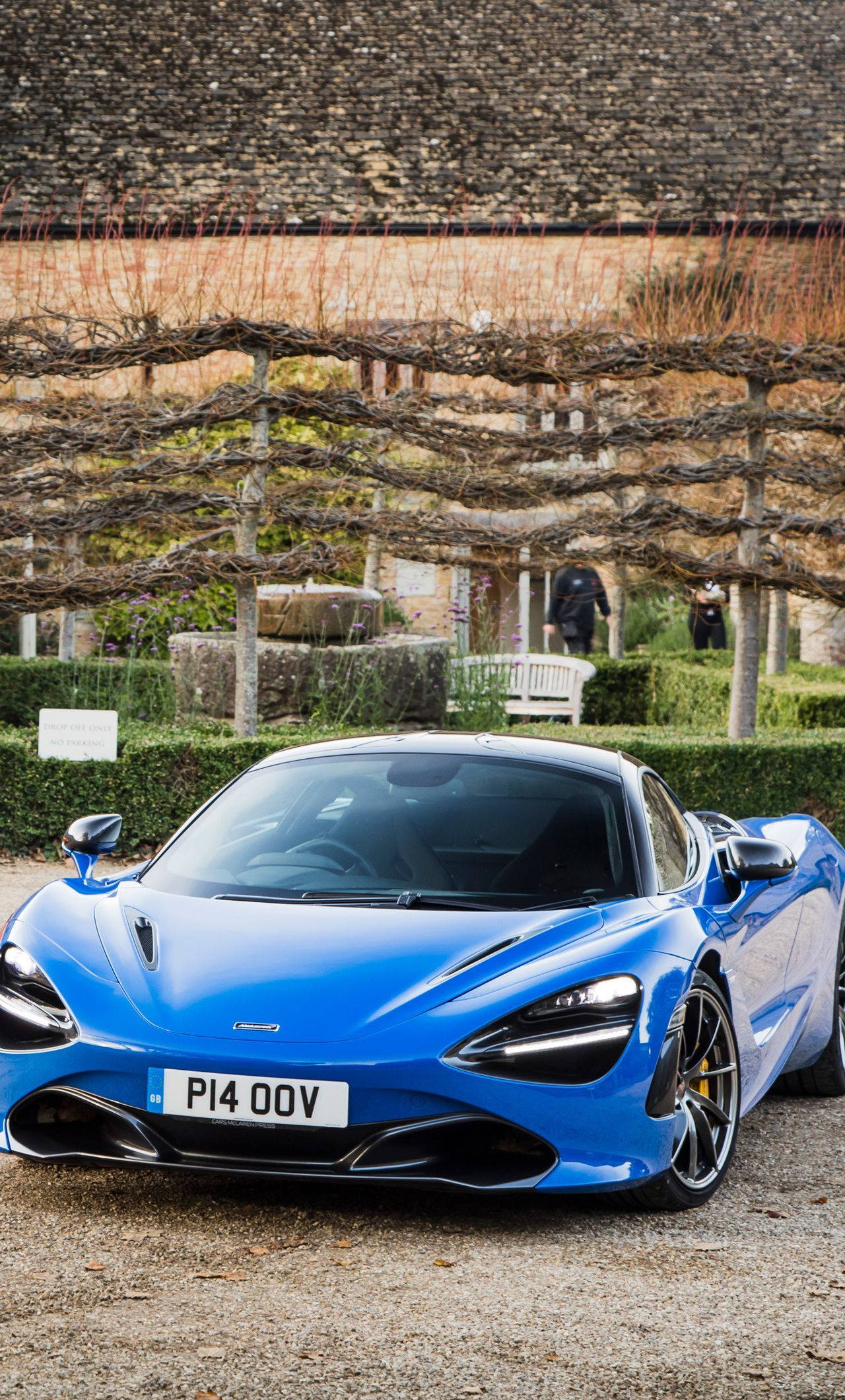 跑車 桌布 壁紙 — 一輛充滿活力的藍色McLaren 720S跑車停泊在碎石路上，周圍是修剪整齊的花園，有石牆和休眠的葡萄藤。