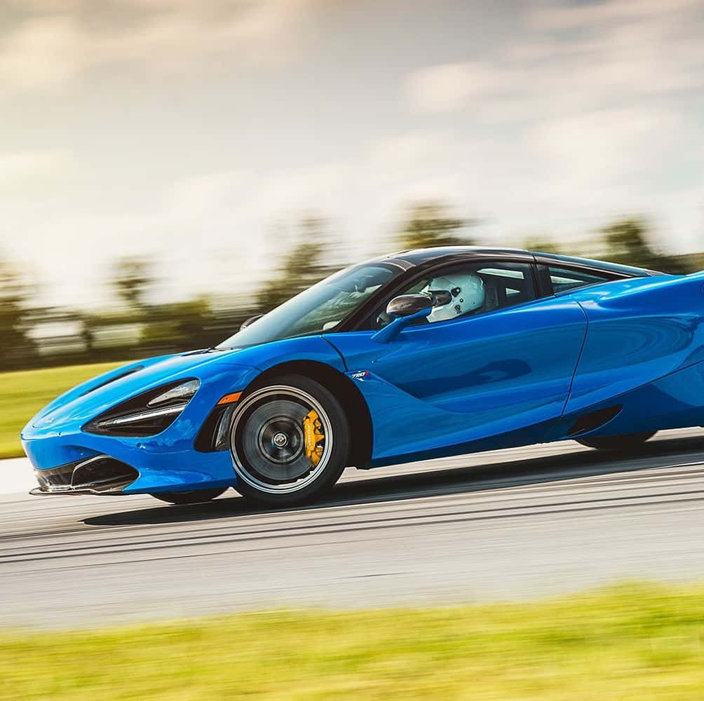 麥拉倫 桌布 壁紙 — 一輛充滿活力的藍色McLaren 720S在道路上疾馳，背景是模糊的綠化和天空。
