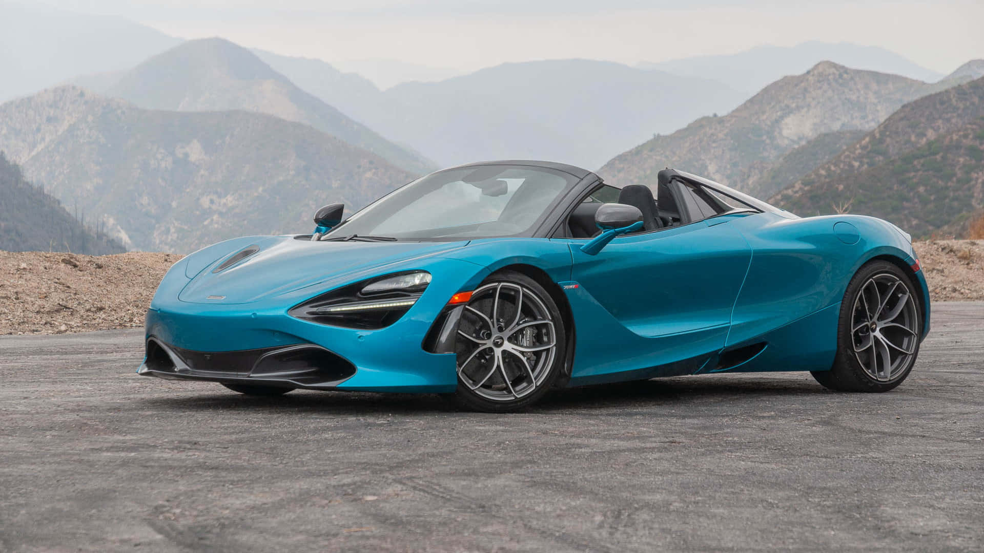 山景 桌布 壁紙 — 一輛充滿活力的藍色McLaren 720S Spider跑車停泊在山路上，背景是崎嶇的山峰。