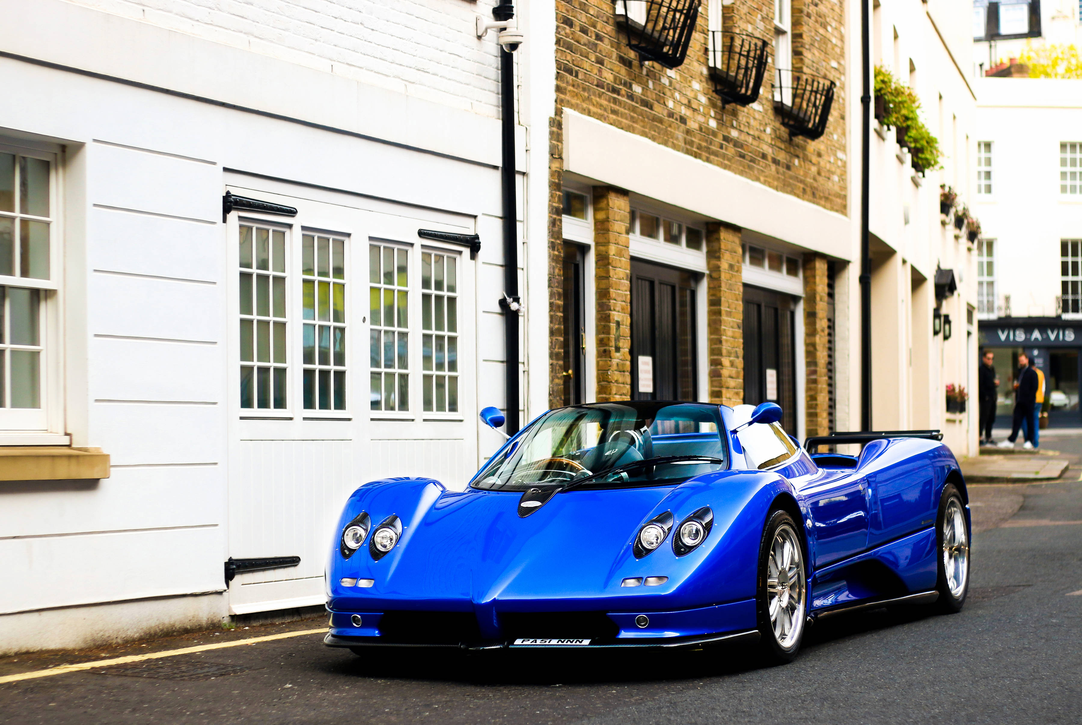 Pagani 桌布 壁紙 — 一輛充滿活力的藍色Pagani Zonda跑車停泊在一條狹窄的城市街道上，兩旁是白色和磚砌的建築物。