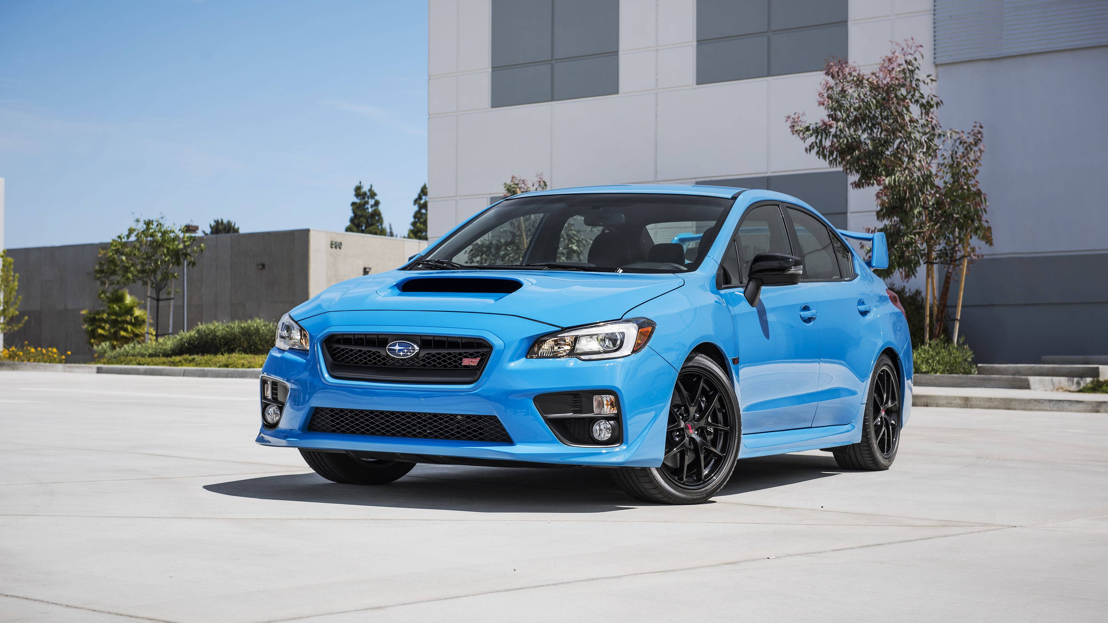 跑車 桌布 壁紙 — 一輛充滿活力的藍色Subaru WRX STI跑車停放在混凝土停車場上，天空清澈湛藍，背景是現代建築。