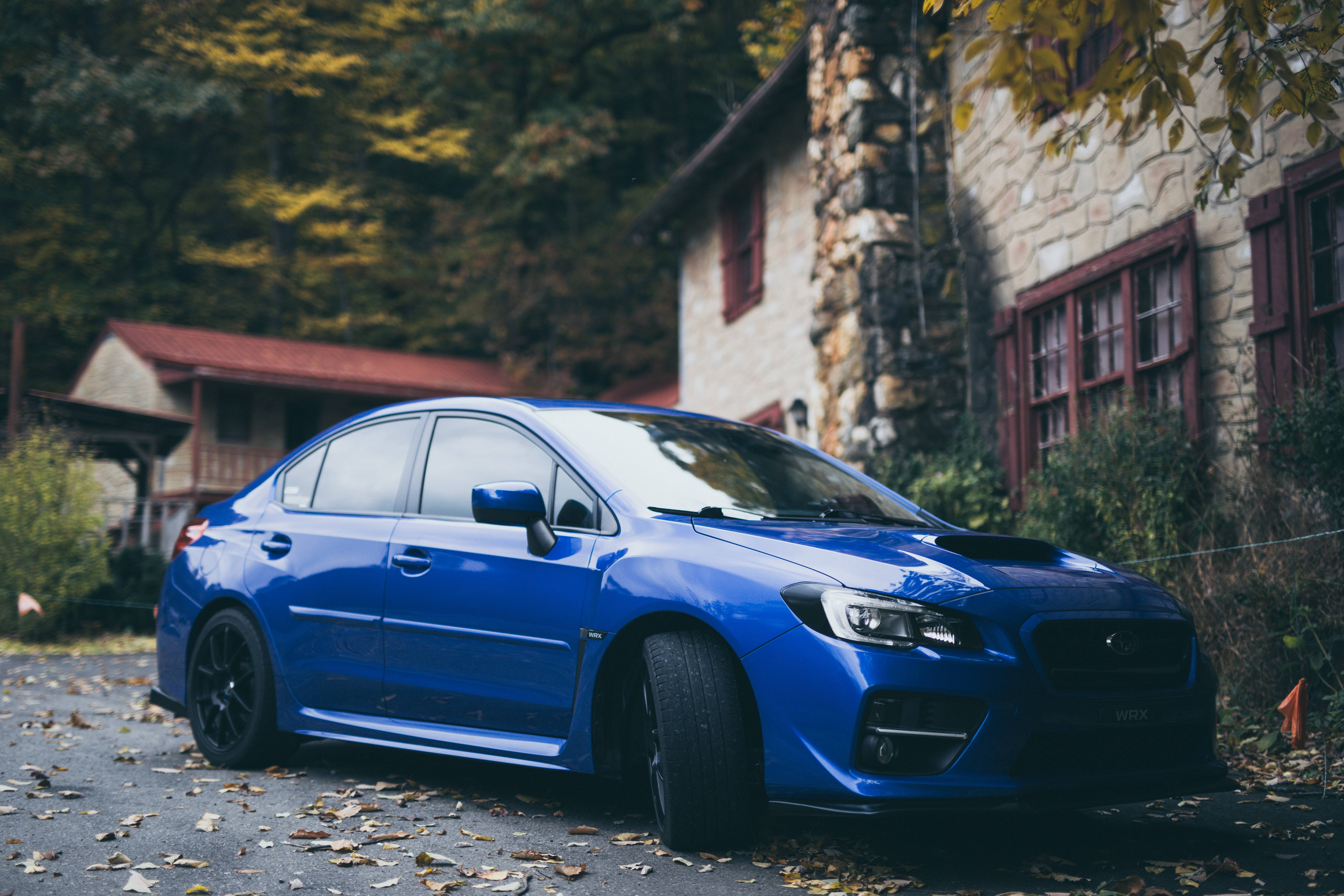 昴 桌布 壁紙 — 一輛充滿活力的藍色Subaru WRX STI停放在落葉滿佈的車道上，旁邊是一座質樸的石屋，正值秋季。