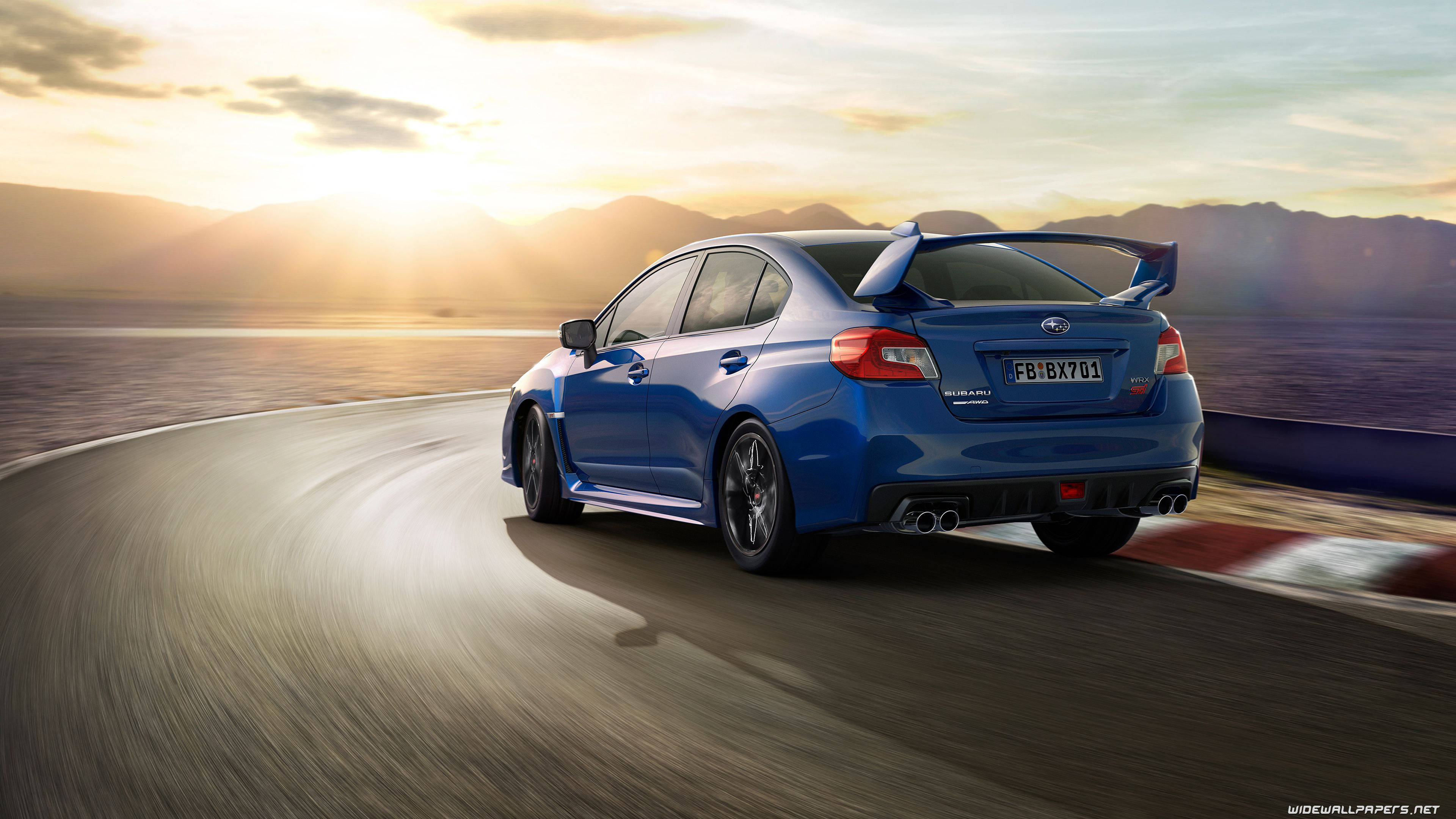 Subaru 桌布 壁紙 — 一輛充滿活力的藍色Subaru WRX STI在日落時分沿著蜿蜒的海岸公路疾馳，背景是山脈。
