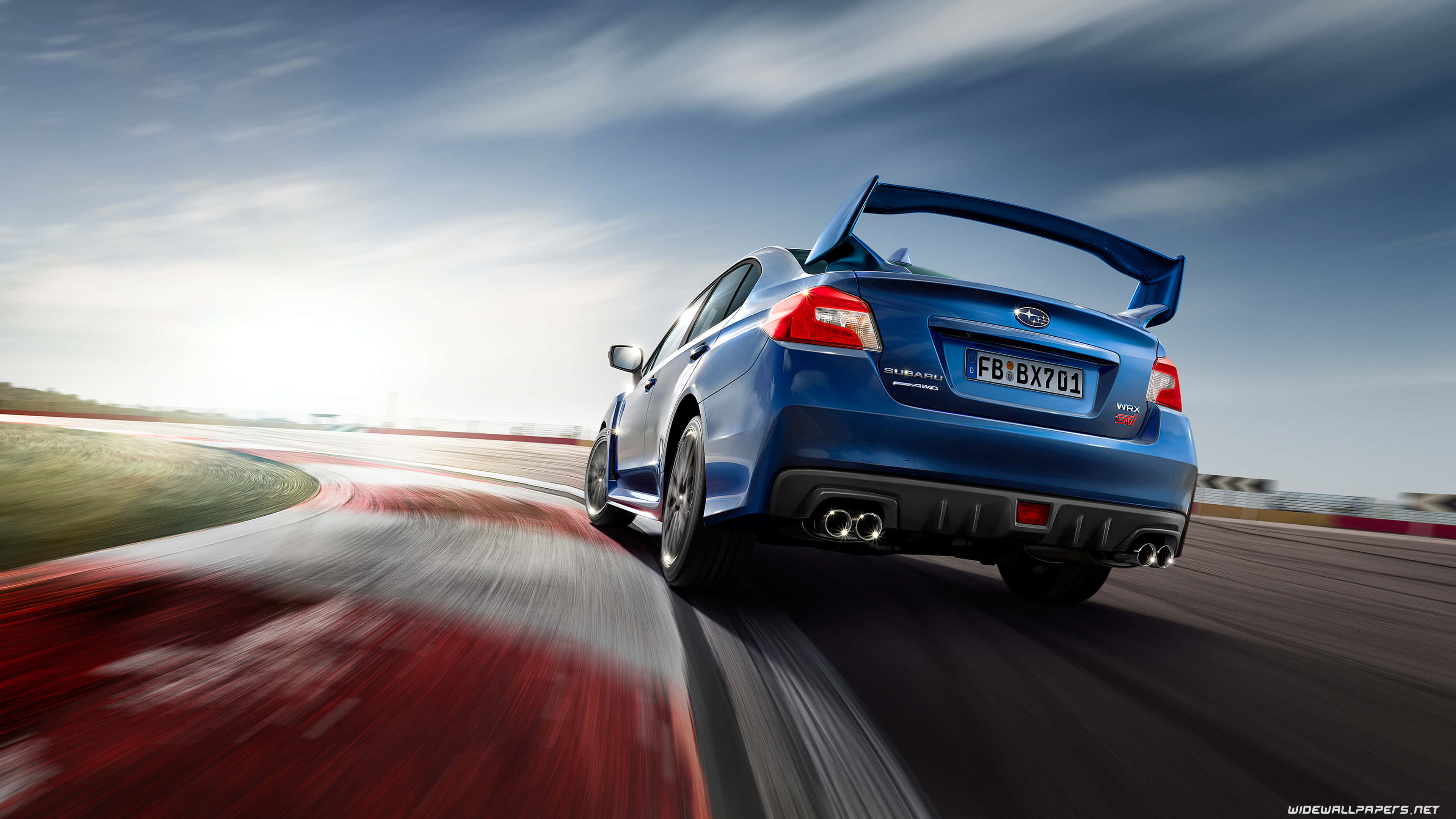 桌布 壁紙 — 一輛充滿活力的藍色Subaru WRX STI在賽道上奔馳，動態模糊效果強調了速度，天空明亮。
