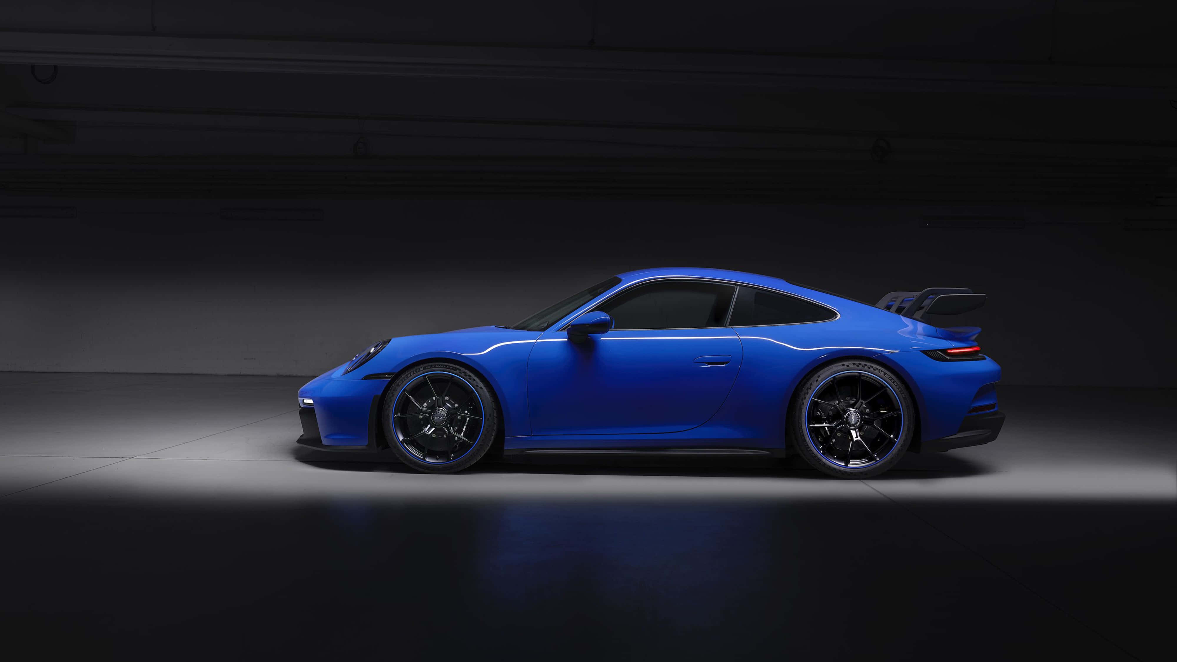 桌布 壁紙 — 一輛充滿活力的藍色保時捷 911 GT3 RS 在極簡風格的暗色車庫中，於攝影棚燈光下閃耀。