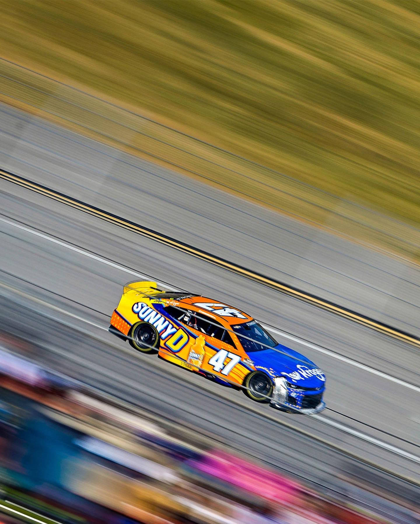 Racing 桌布 壁紙 — 一輛充滿活力的藍色和橙色NASCAR賽車在賽道上疾馳，背景帶有動態模糊效果。