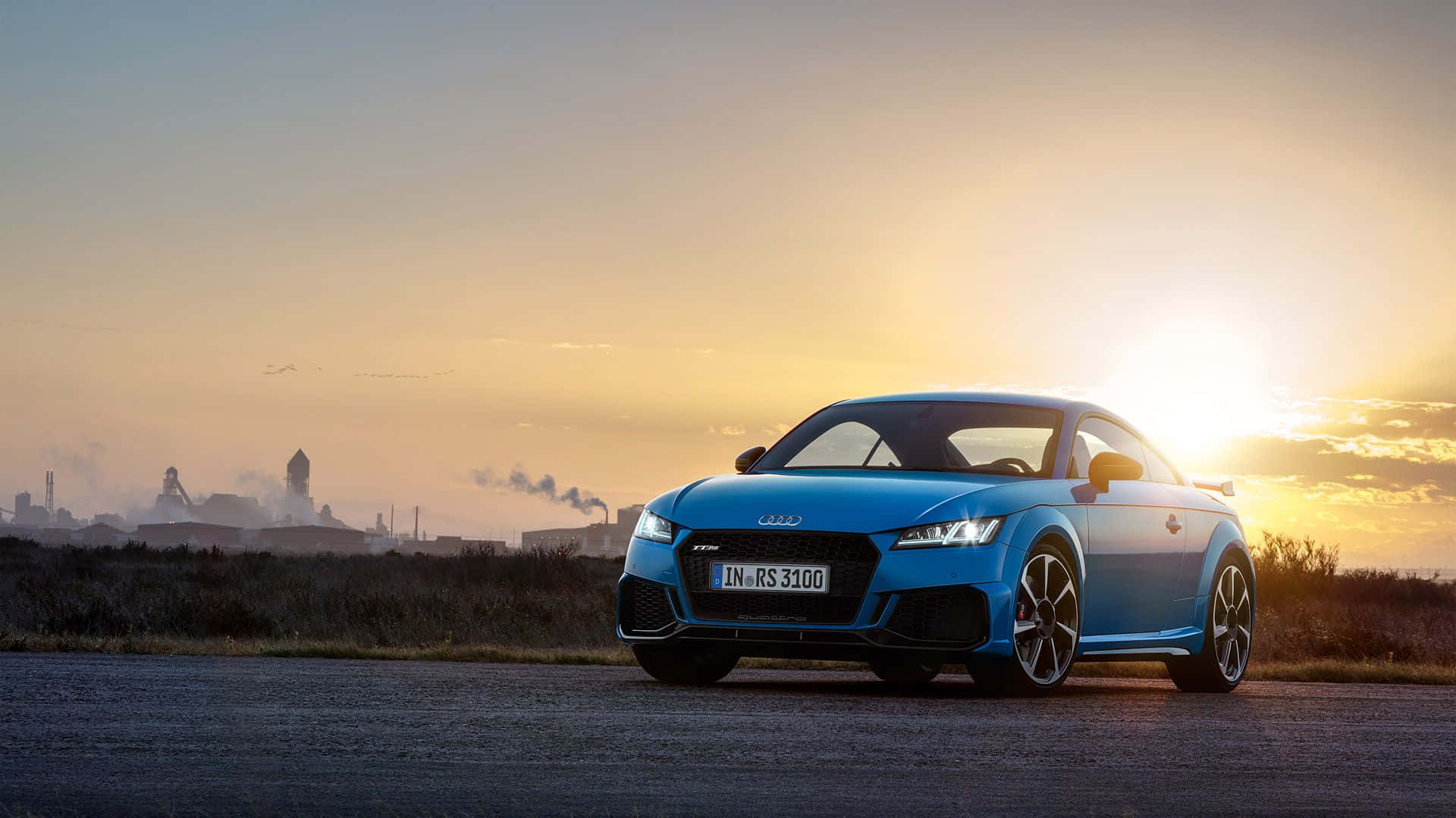 Audi Tt 桌布 壁紙 — 一輛充滿活力的藍色奧迪 TT RS 3100 停在日落時分的瀝青路上，背景是工業煙囪。