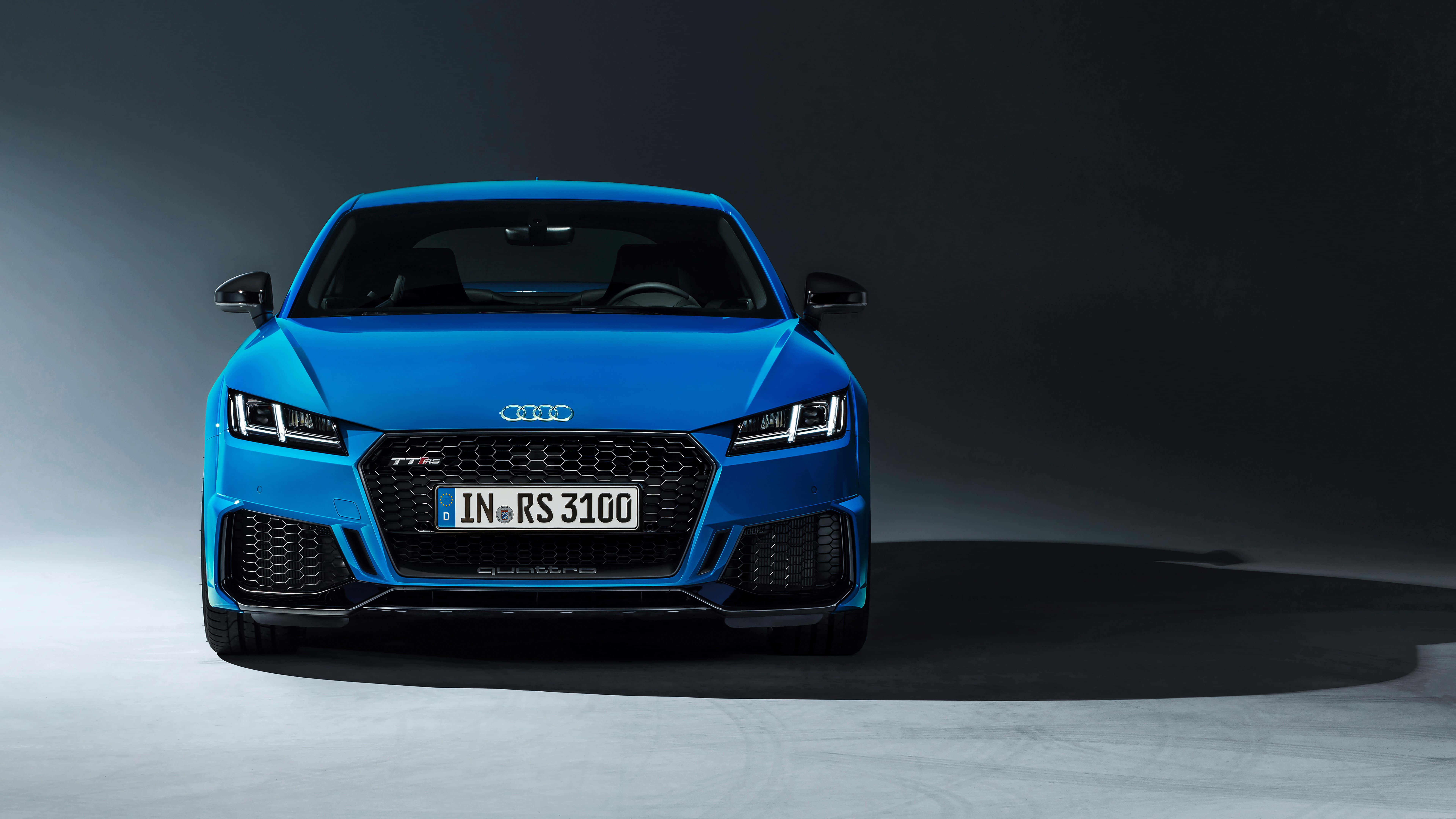Audi Tt 桌布 壁紙 — 一輛充滿活力的藍色奧迪TT RS 3100跑車在極簡風格的工作室中，以戲劇性的燈光和深色背景正面朝前。
