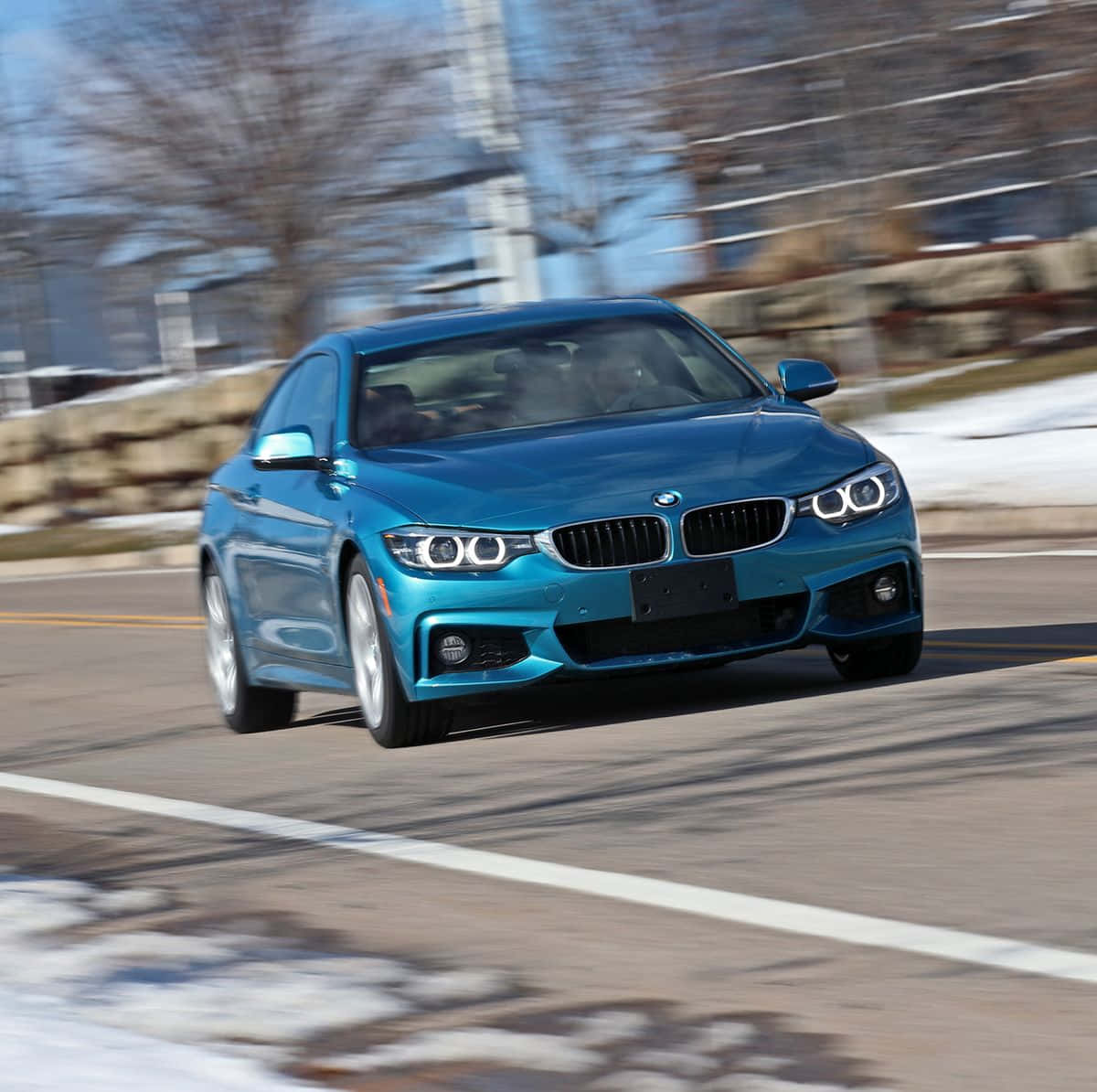 Bmw 440i 桌布 壁紙 — 一輛充滿活力的藍色寶馬轎跑車在積雪的路邊飛馳，背景是模糊的冬季樹木和建築物。