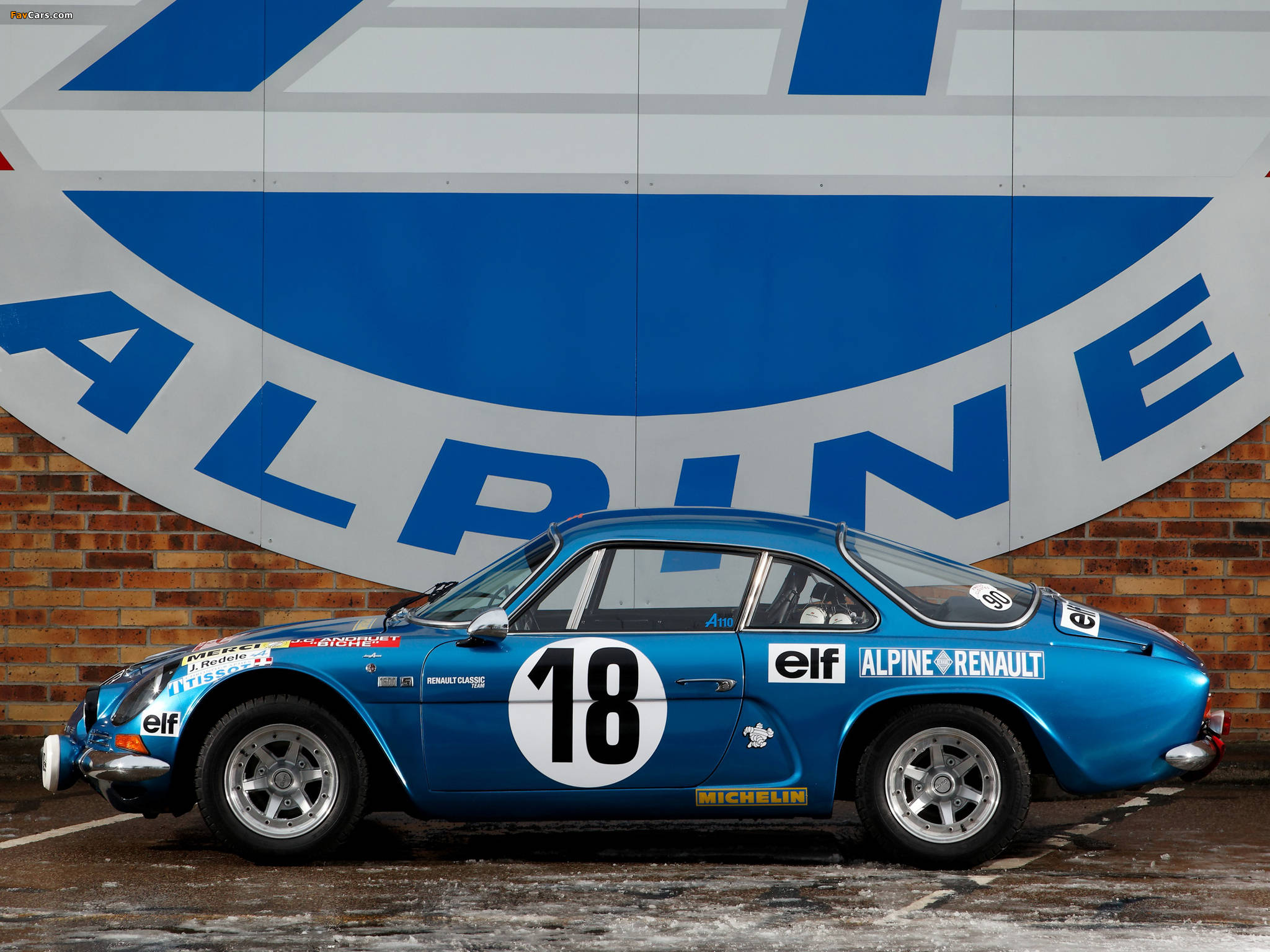 F1 桌布 壁紙 — 一輛充滿活力的藍色復古Alpine A110賽車，車號18，停在磚牆上一個大型Alpine標誌前。