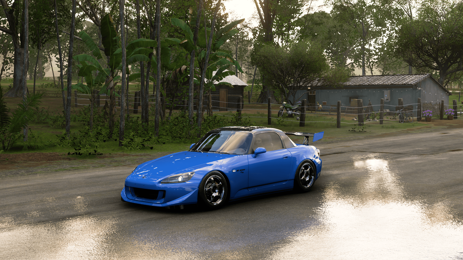 Forza 桌布 壁紙 — 一輛充滿活力的藍色改裝跑車在黎明時分沿著一條濕潤的鄉村道路滑行，兩旁是茂密的綠樹和質樸的小屋。