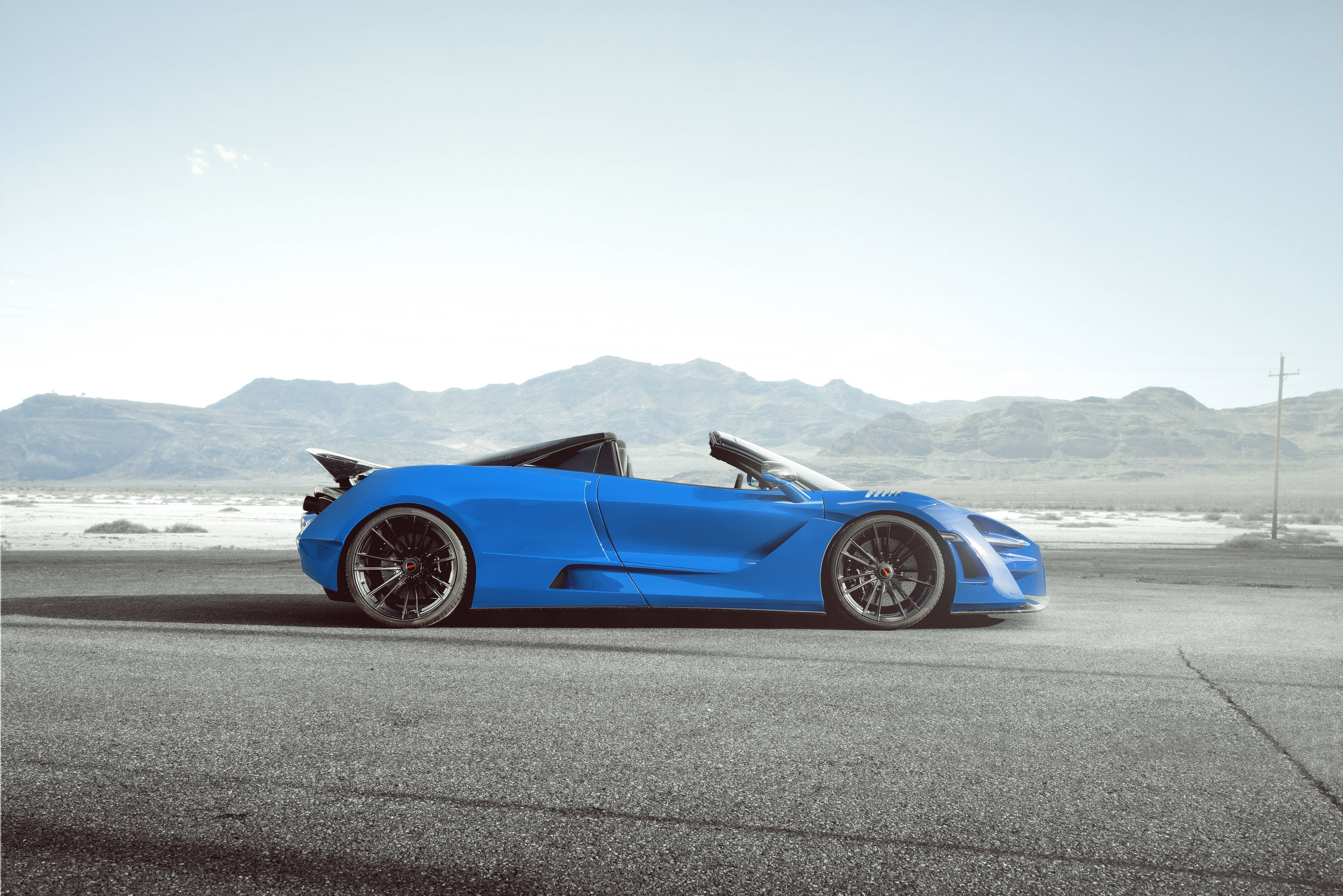 mclaren 720s 4K 桌布 壁紙 — 一輛充滿活力的藍色敞篷跑車停放在空曠的沙漠公路上，遠山在朦朧的天空下若隱若現。