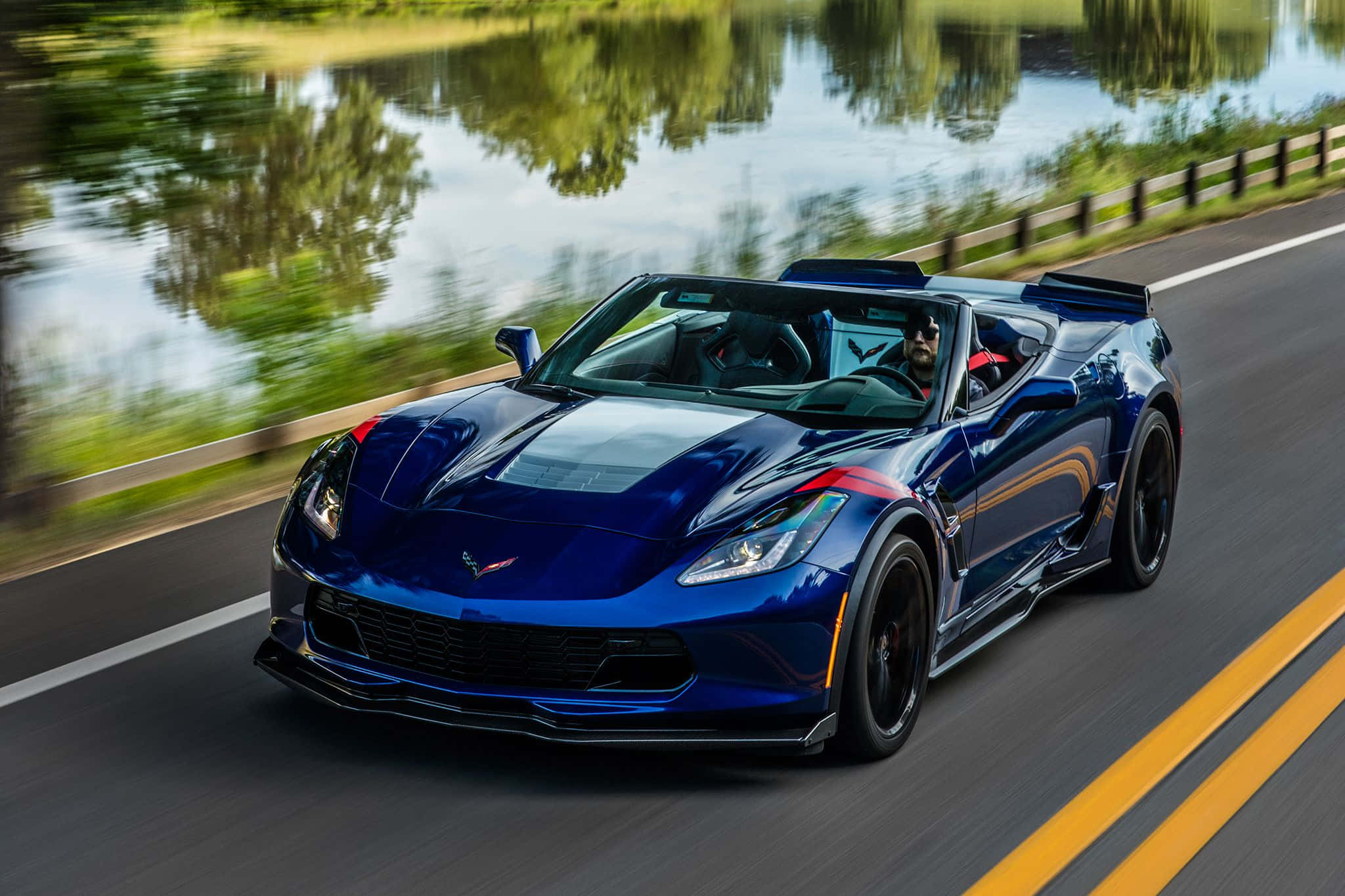 Chevrolet Corvette Grand Sport 桌布 壁紙 — 一輛充滿活力的藍色敞篷跑車沿著路邊飛馳，背景是模糊的綠色河岸。