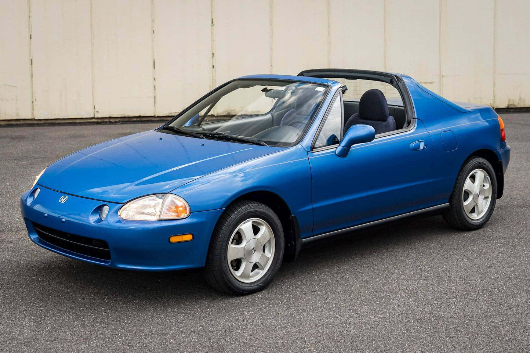 Honda Civic Del Sol 桌布 壁紙 — 一輛充滿活力的藍色本田Del Sol敞篷車停在瀝青路上，後面是一面純米色牆壁。