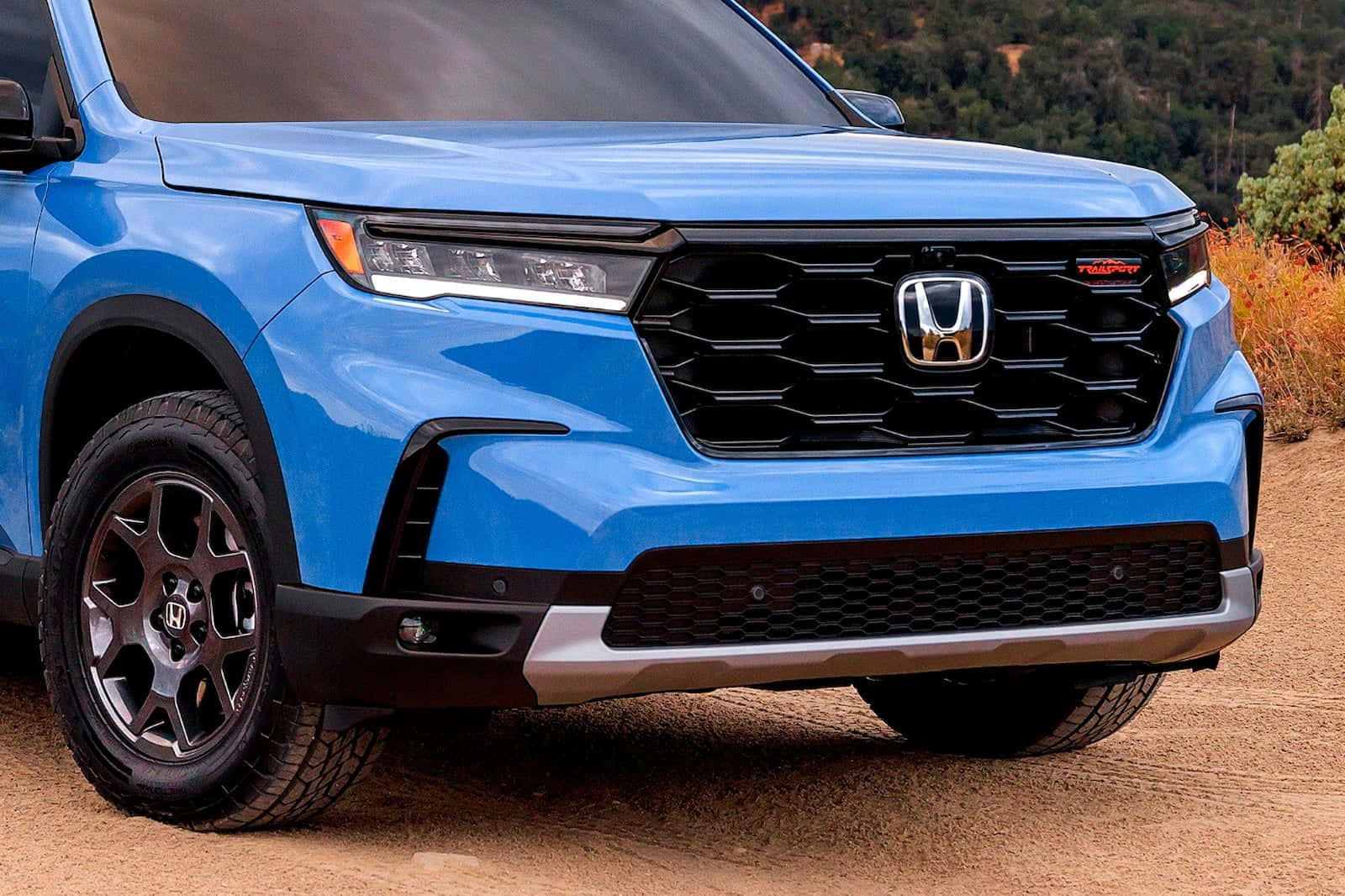 2023 Honda Pilot 桌布 壁紙 — 一輛充滿活力的藍色本田SUV，帶有黑色飾邊和堅固輪胎，停泊在泥路上，背景是森林覆蓋的山丘。