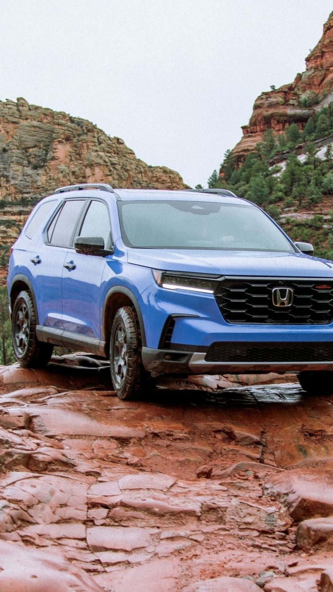 2023 Honda Pilot 桌布 壁紙 — 一輛充滿活力的藍色本田SUV在多雲的天空下穿越崎嶇的紅色岩石地形。