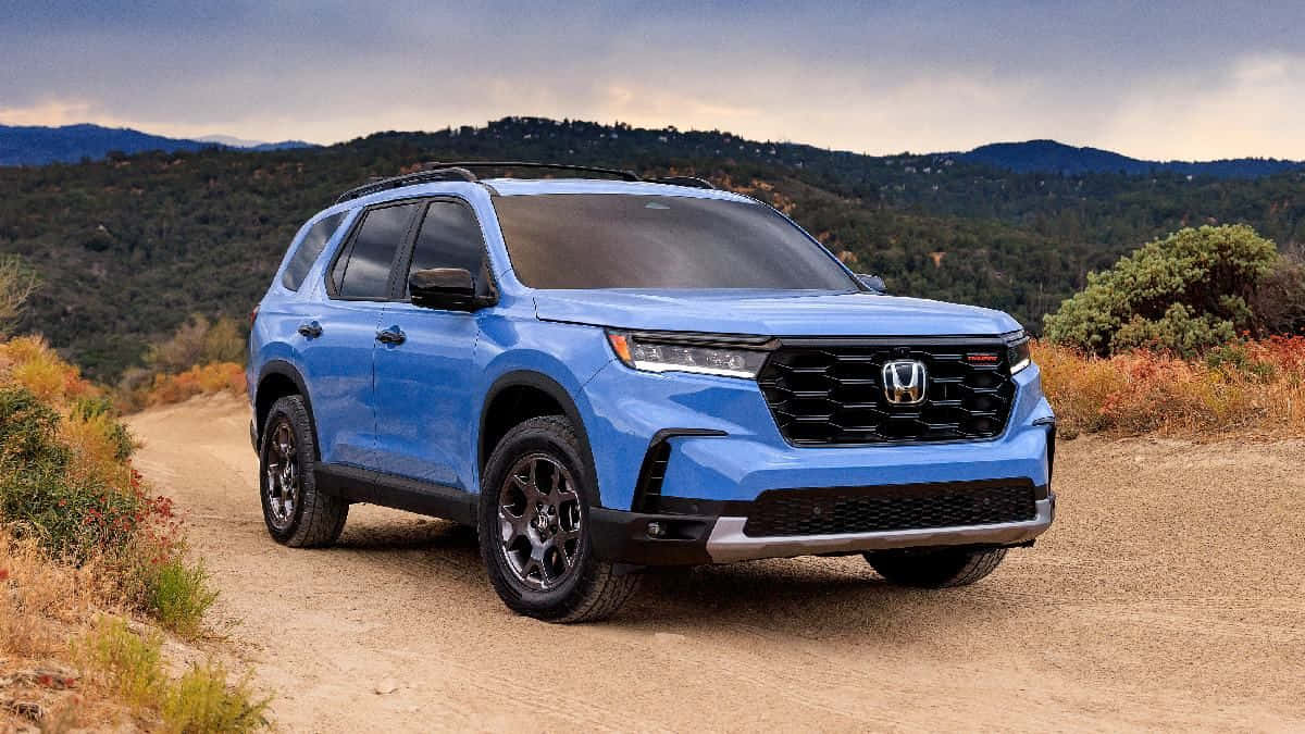 2023 Honda Pilot 桌布 壁紙 — 一輛充滿活力的藍色本田SUV在陰天下的塵土飛揚的山路上自信地行駛。