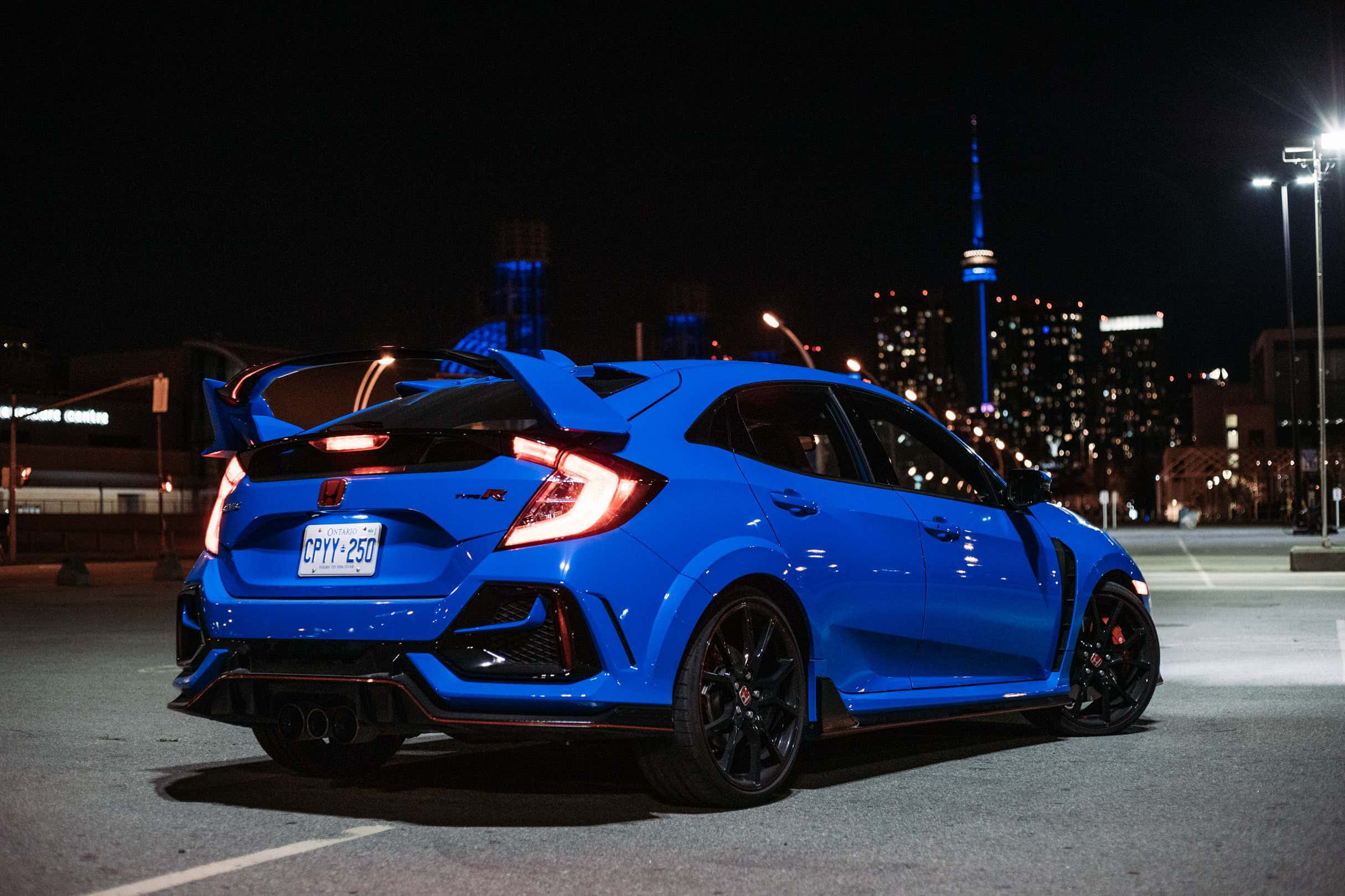 Hatchback 桌布 壁紙 — 一輛充滿活力的藍色本田思域Type R在夜間停車，尾燈發光，背景是包括CN塔的城市天際線。