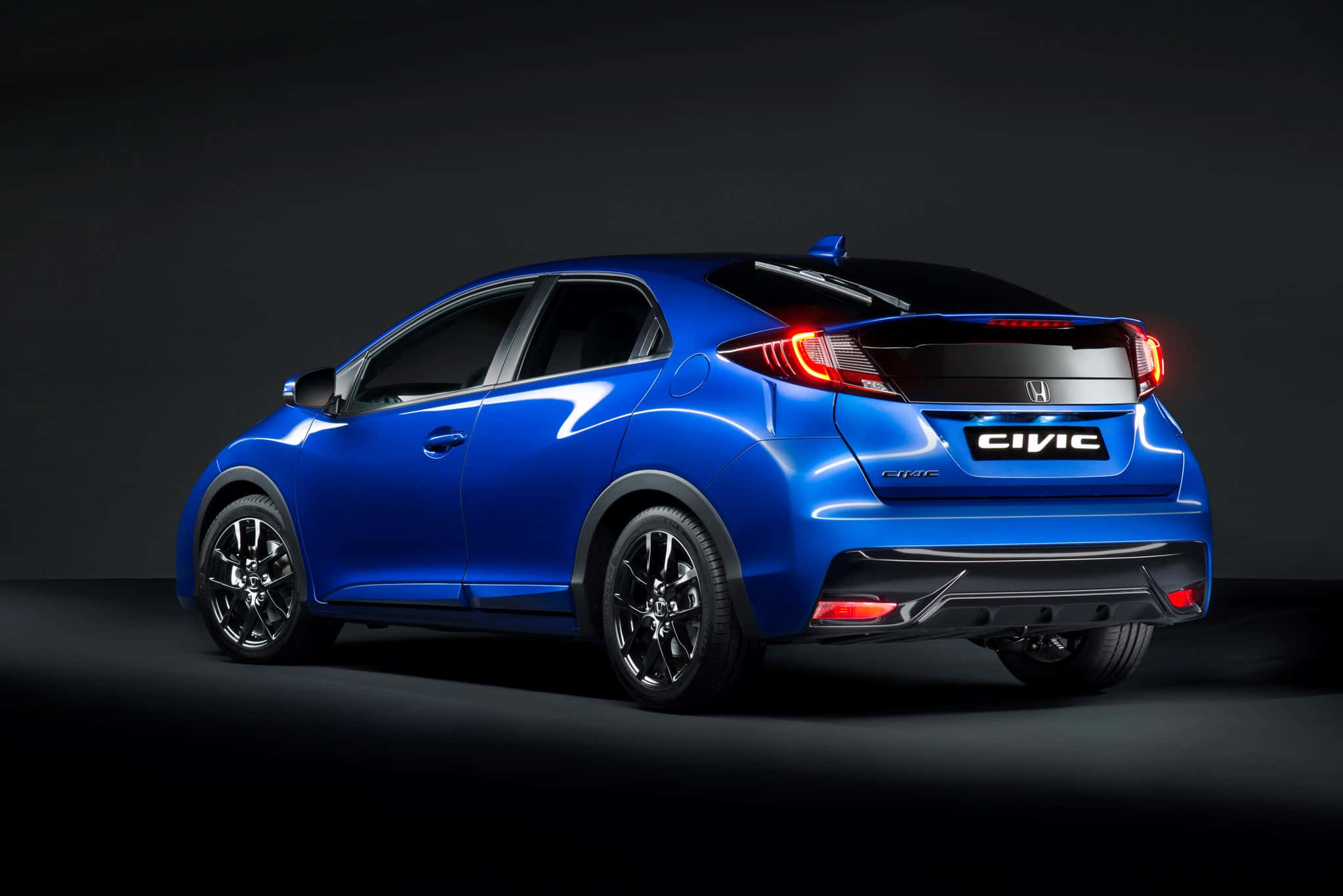 Honda Civic 桌布 壁紙 — 一輛充滿活力的藍色本田思域掀背車在攝影棚燈光下閃閃發光，紅色尾燈在黑暗背景下發光。