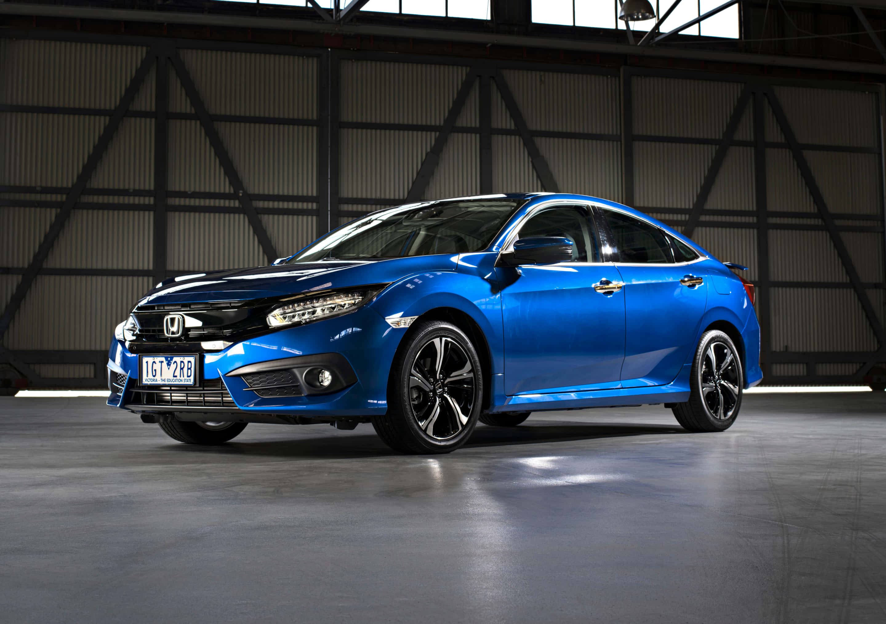 Honda Civic 桌布 壁紙 — 一輛充滿活力的藍色本田思域轎車在寬敞的工業倉庫內，在裸露鋼樑下的攝影棚燈光中閃閃發光。