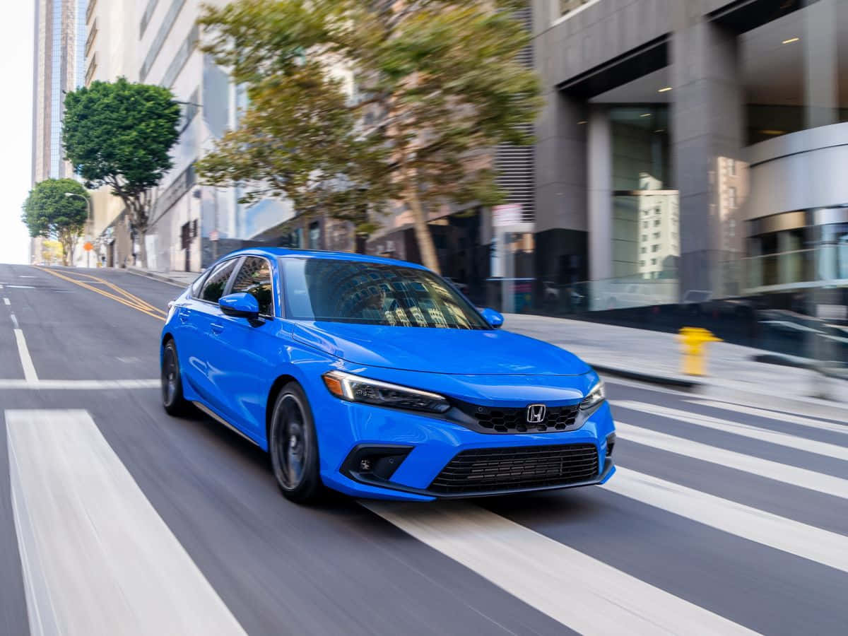 Honda Civic 桌布 壁紙 — 一輛充滿活力的藍色本田轎車在城市的街道上奔馳，路面呈現動態模糊，背景是現代建築。