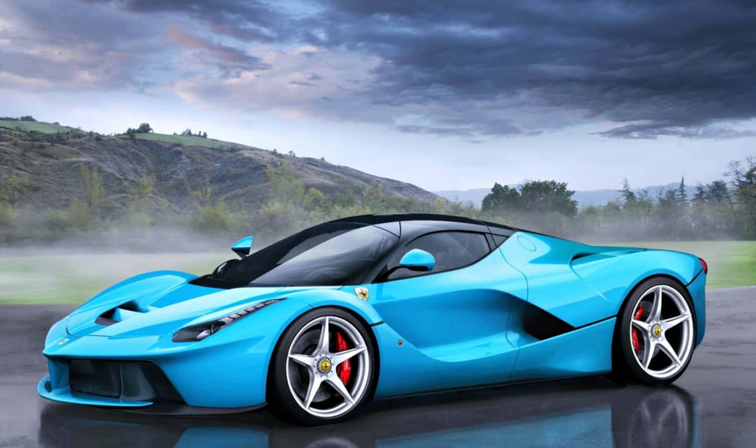 法拉利 桌布 壁紙 — 一輛充滿活力的藍色法拉利 LaFerrari 跑車在潮濕的道路上閃閃發光，背景是戲劇性的多雲天空和霧氣瀰漫的山丘。