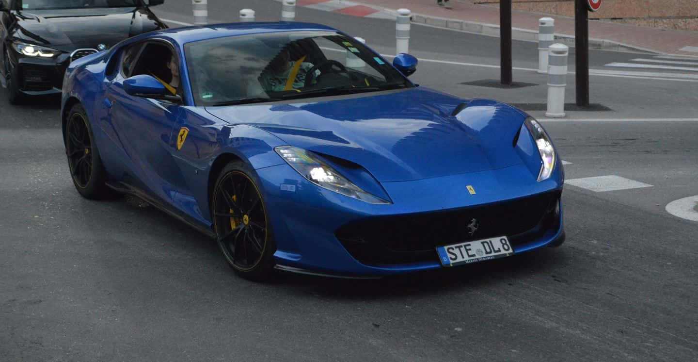 Ferrari 812 Superfast 桌布 壁紙 — 一輛充滿活力的藍色法拉利跑車帶有黃色點綴，在城市的街道上行駛，附近有另一輛車。