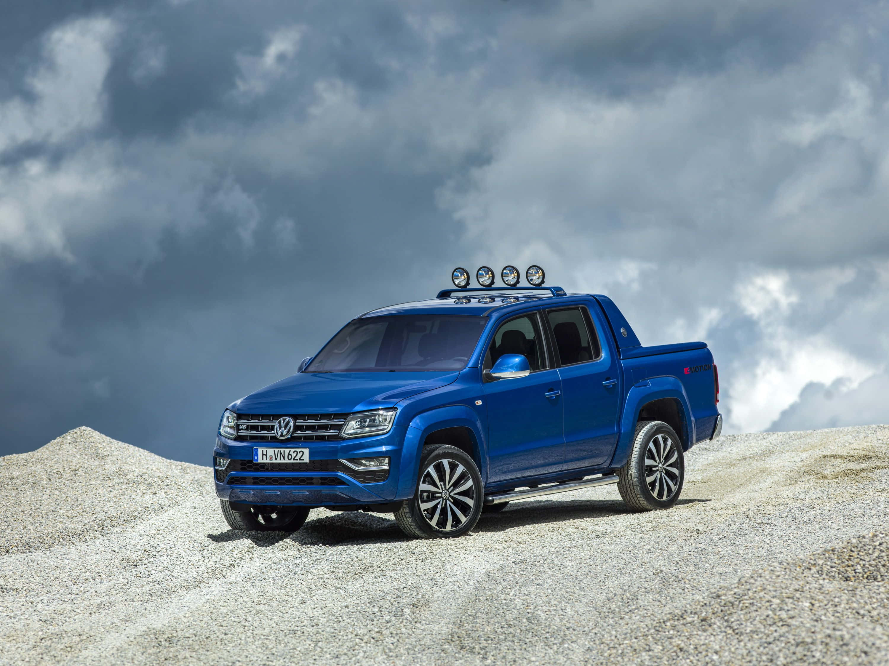 桌布 壁紙 — 一輛充滿活力的藍色福斯Amarok pickup貨車，在戲劇性的多雲天空下，停泊在碎石山丘上。