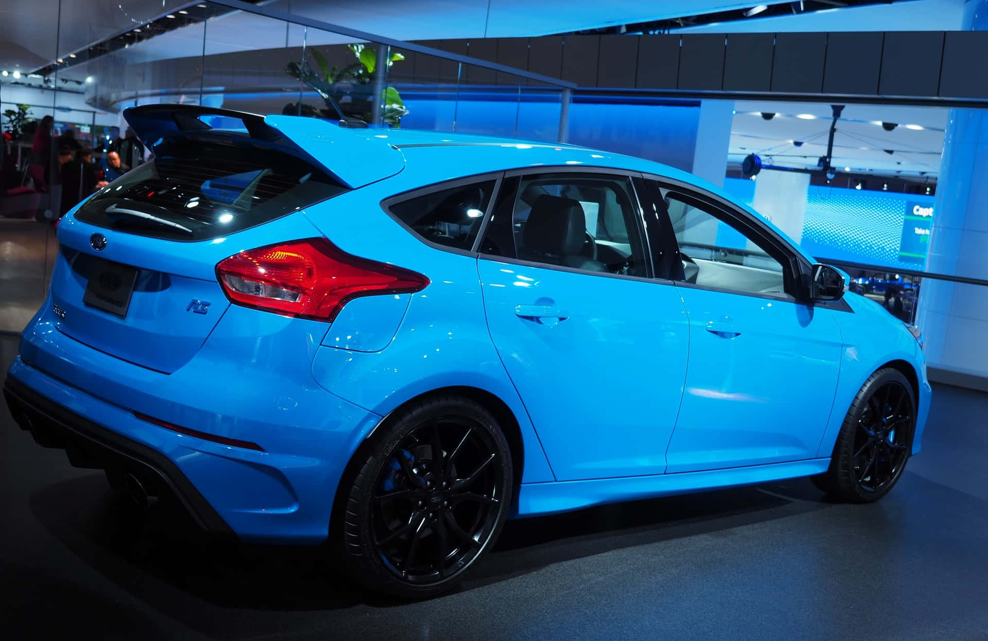 Ford Focus 桌布 壁紙 — 一輛充滿活力的藍色福特福克斯RS掀背車在展廳燈光下閃閃發光，配備黑色輪圈和後擾流板。