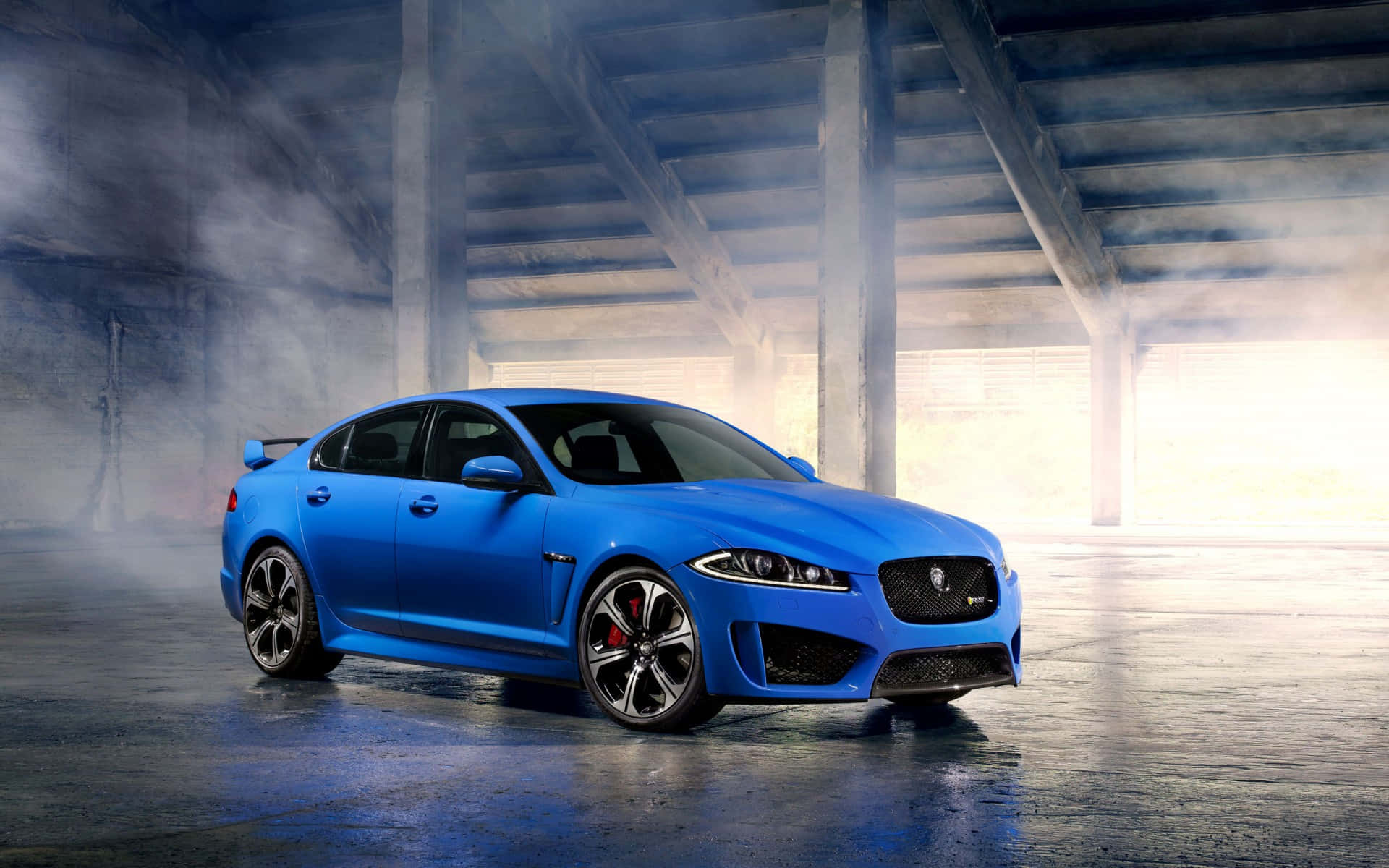 Jaguar Xfr 桌布 壁紙 — 一輛充滿活力的藍色積架跑車在霧氣瀰漫的混凝土地下道中，在工業橫樑下戲劇性的燈光下閃閃發光。