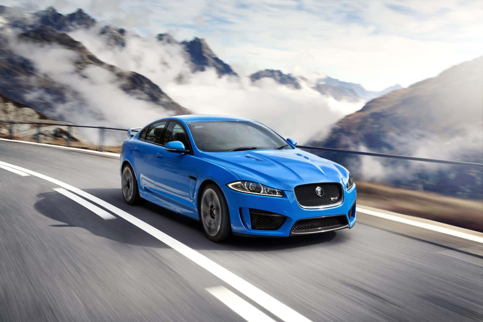 Jaguar Xfr 桌布 壁紙 — 一輛充滿活力的藍色積架跑車沿著山路疾馳，雲霧在崎嶇的山峰下翻滾。