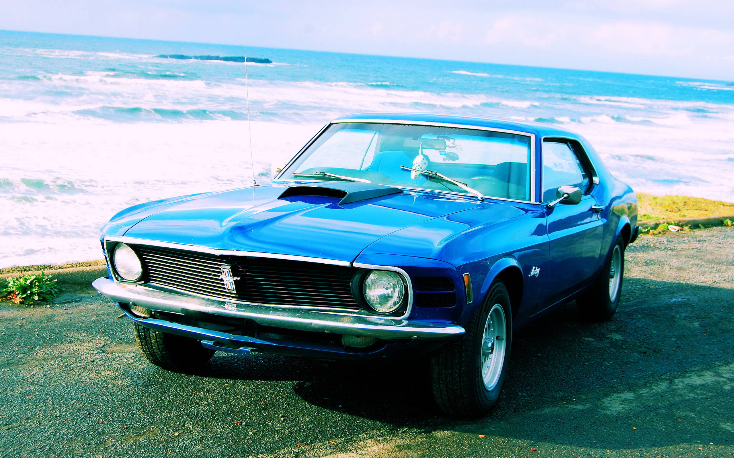 mustang HD 桌布 壁紙 — 一輛充滿活力的藍色經典肌肉車停泊在沿海公路上，背後是洶湧的海浪。
