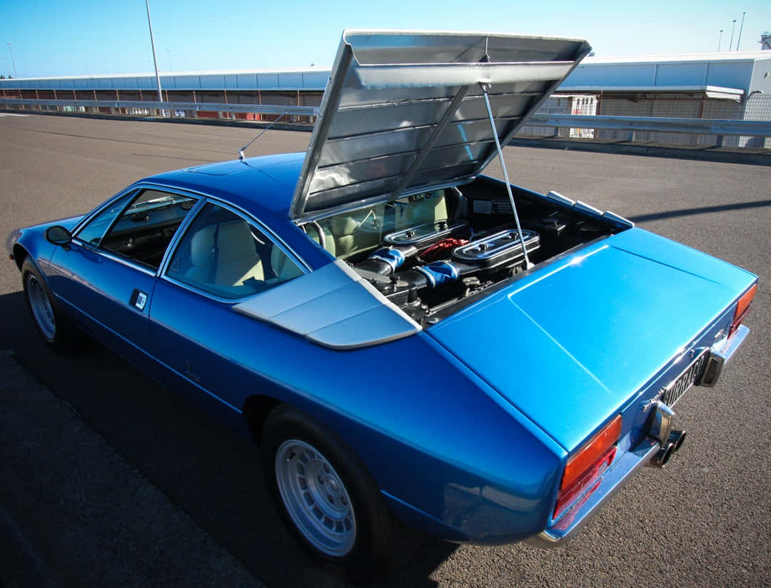 Lamborghini Urraco 桌布 壁紙 — 一輛充滿活力的藍色經典跑車，在晴朗的天空下，引擎室暴露在瀝青賽道上。