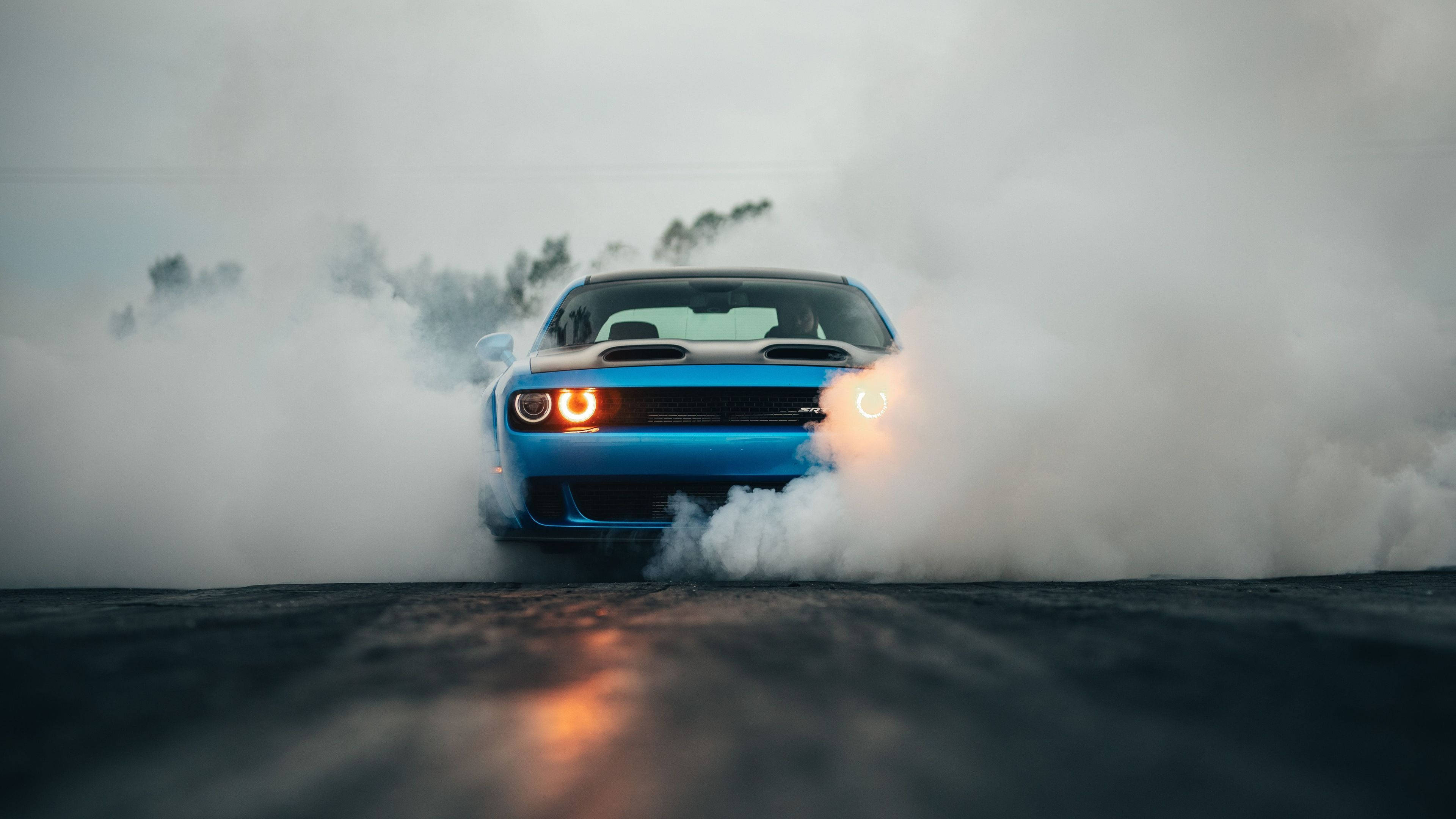 Challenger 桌布 壁紙 — 一輛充滿活力的藍色肌肉車在潮濕的瀝青路上進行燒胎，被濃厚的白煙和發光的橙色車頭燈包圍。