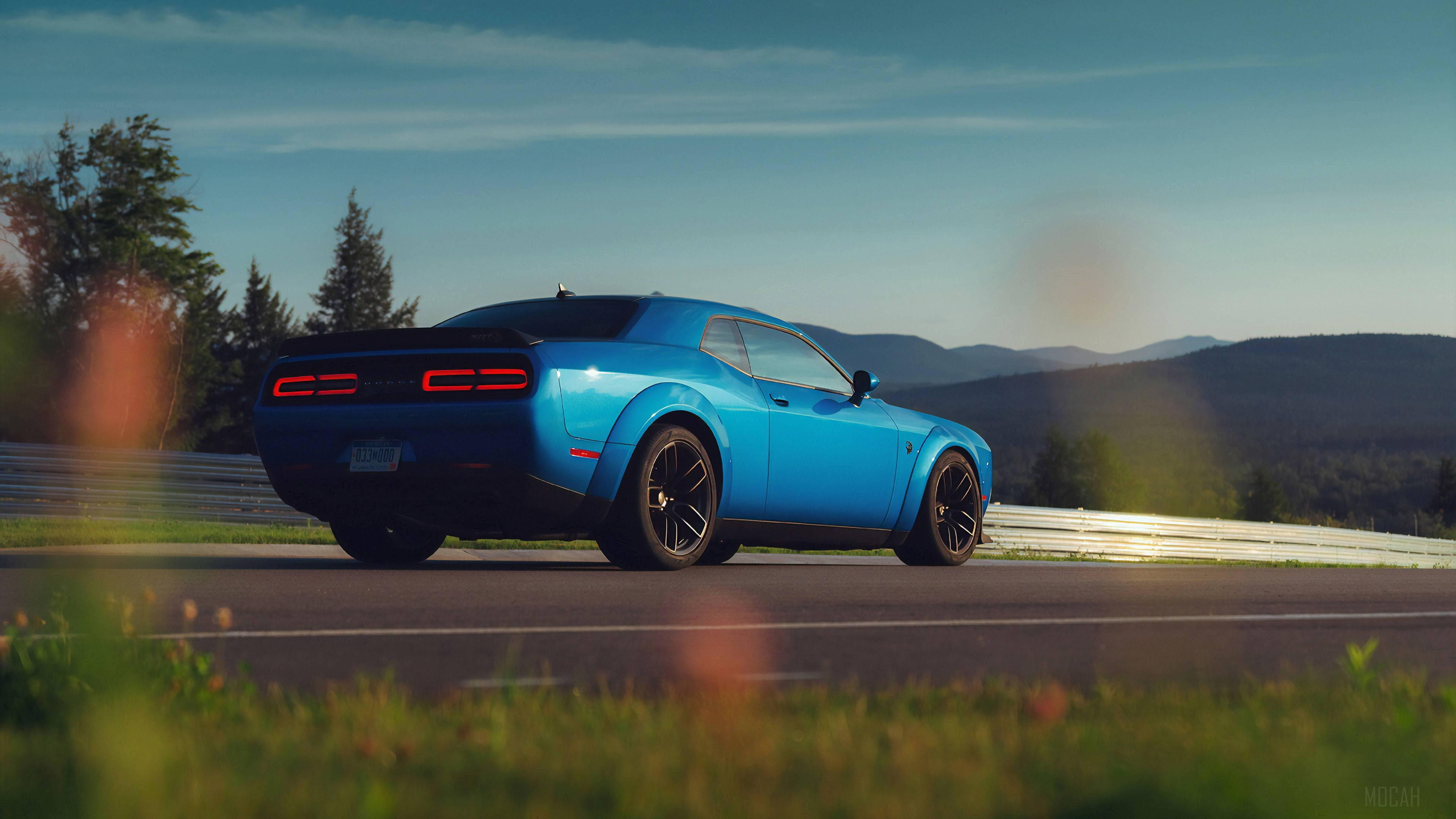 Dodge 桌布 壁紙 — 一輛充滿活力的藍色肌肉車在黃金時段沿著蜿蜒的山路行駛，前景的草地模糊不清。