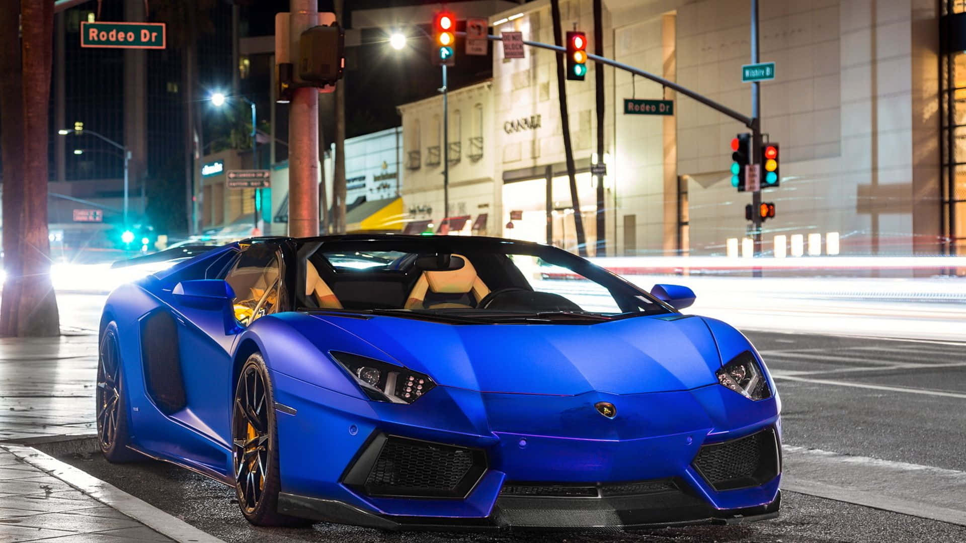 跑車 桌布 壁紙 — 一輛充滿活力的藍色藍寶堅尼 Aventador Roadster 在夜晚繁華的城市街道上，在霓虹燈下閃閃發光。