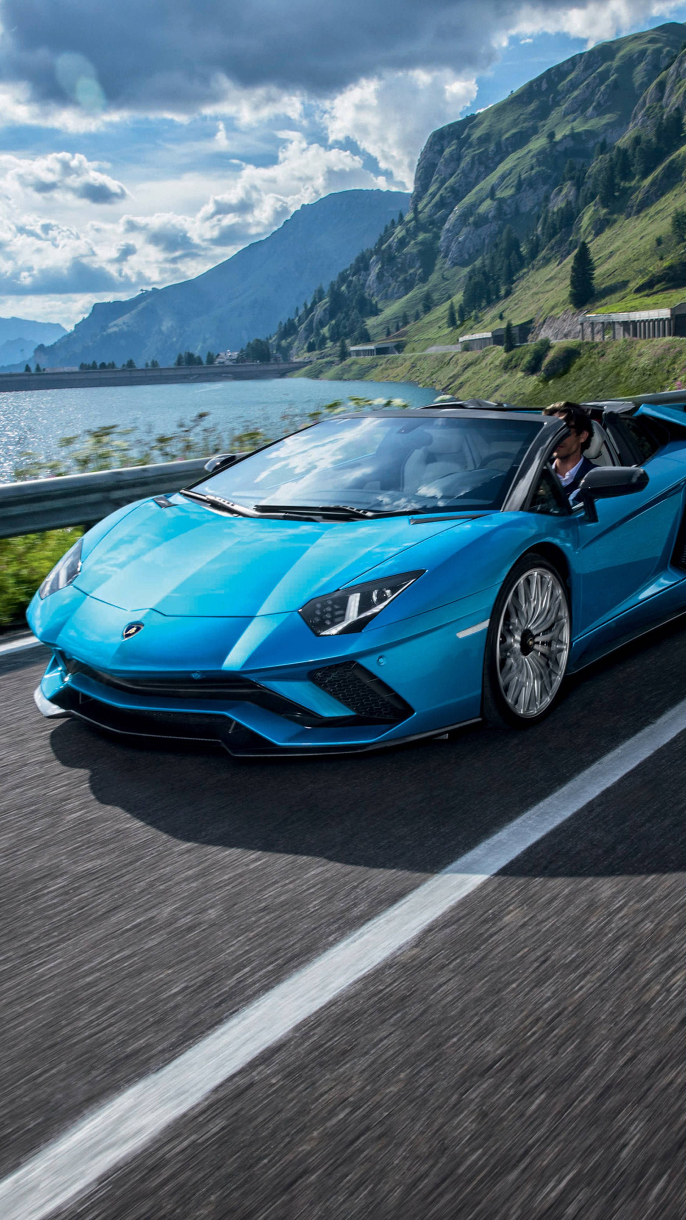 蘭博基尼 桌布 壁紙 — 一輛充滿活力的藍色藍寶堅尼Aventador敞篷跑車，在部分多雲的天空下，沿著湖邊的山路疾馳。