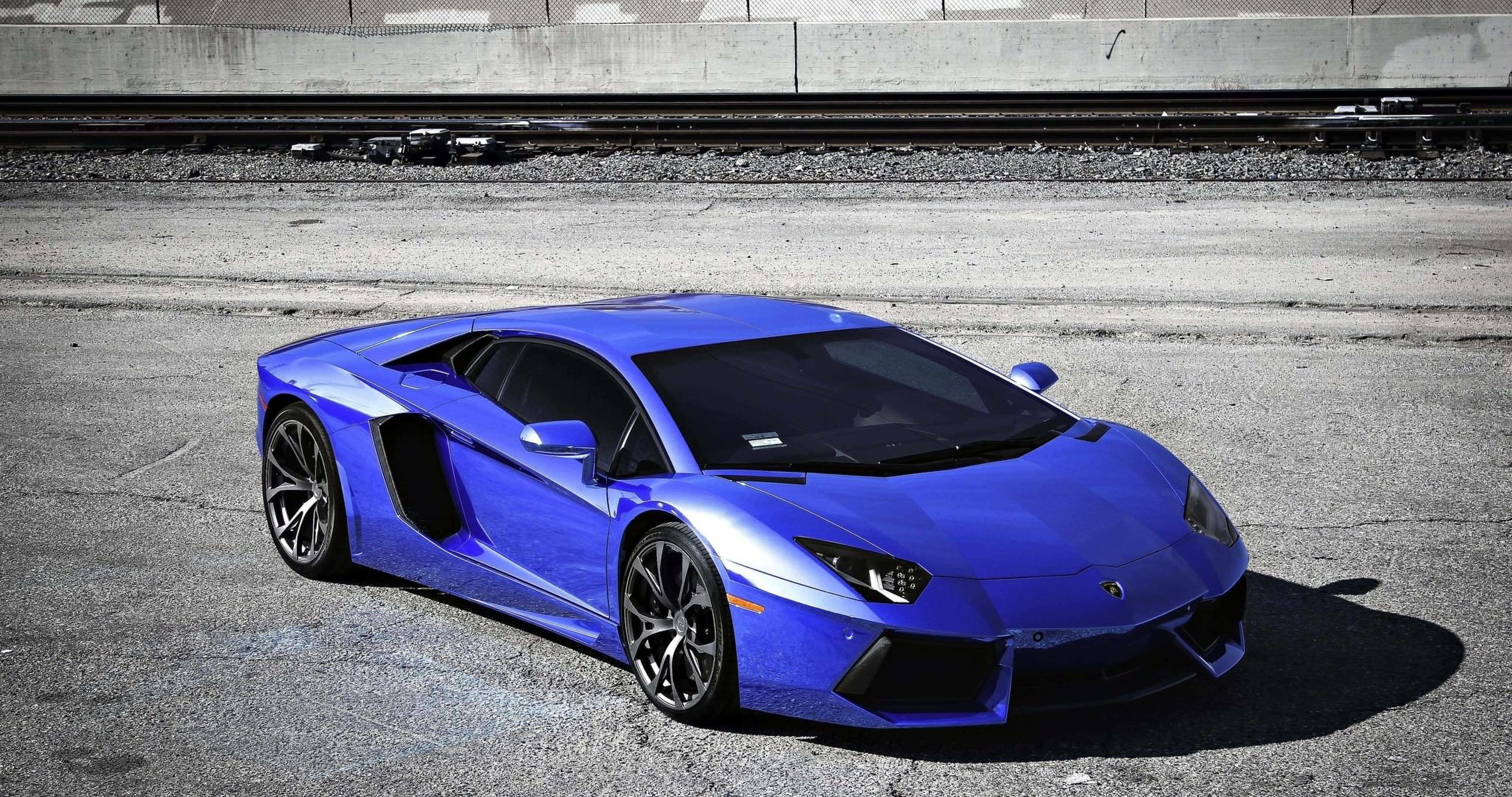 跑車 桌布 壁紙 — 一輛充滿活力的藍色藍寶堅尼Aventador超級跑車在明亮的日光下停泊在裂開的柏油路上。