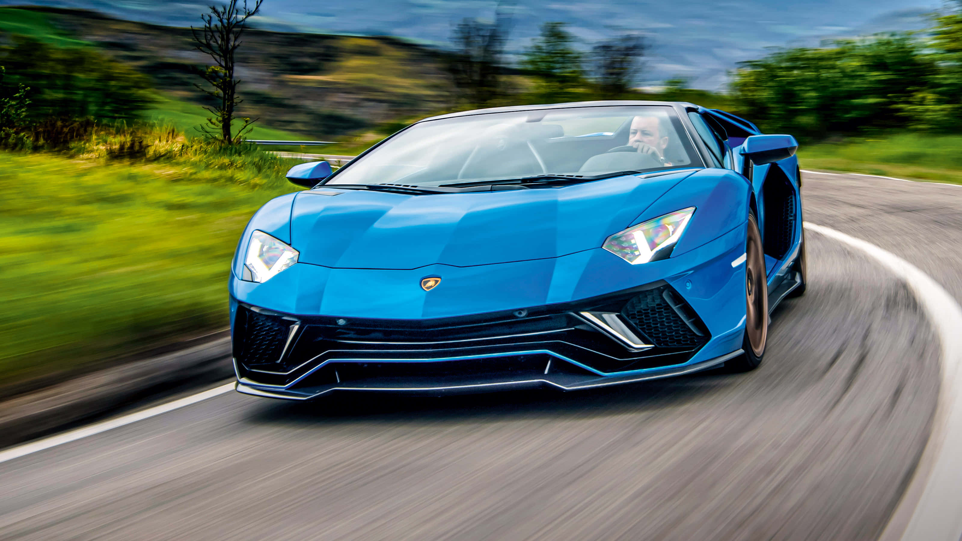 Lamborghini Aventador 桌布 壁紙 — 一輛充滿活力的藍色藍寶堅尼Aventador在蜿蜒的鄉村道路上疾馳，周圍帶有動態模糊效果。