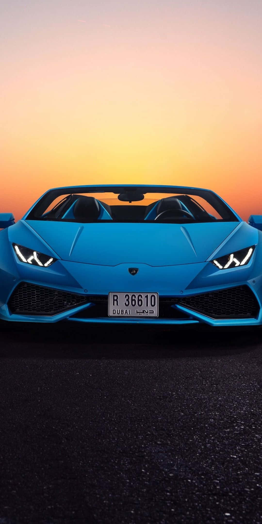 Pixel 3 Lamborghini 桌布 壁紙 — 一輛充滿活力的藍色藍寶堅尼Huracán Spyder在深色路面上向前，背景是溫暖的橙色和黃色日落天空。