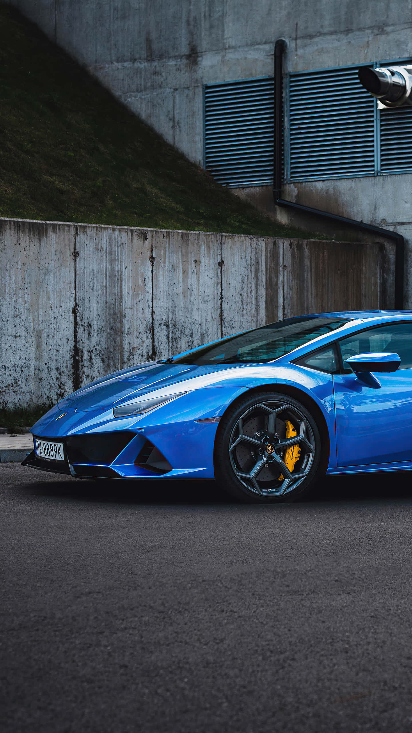 Blue Car 桌布 壁紙 — 一輛充滿活力的藍色藍寶堅尼Huracán跑車停靠在風化的混凝土牆旁，帶有綠色斜坡。