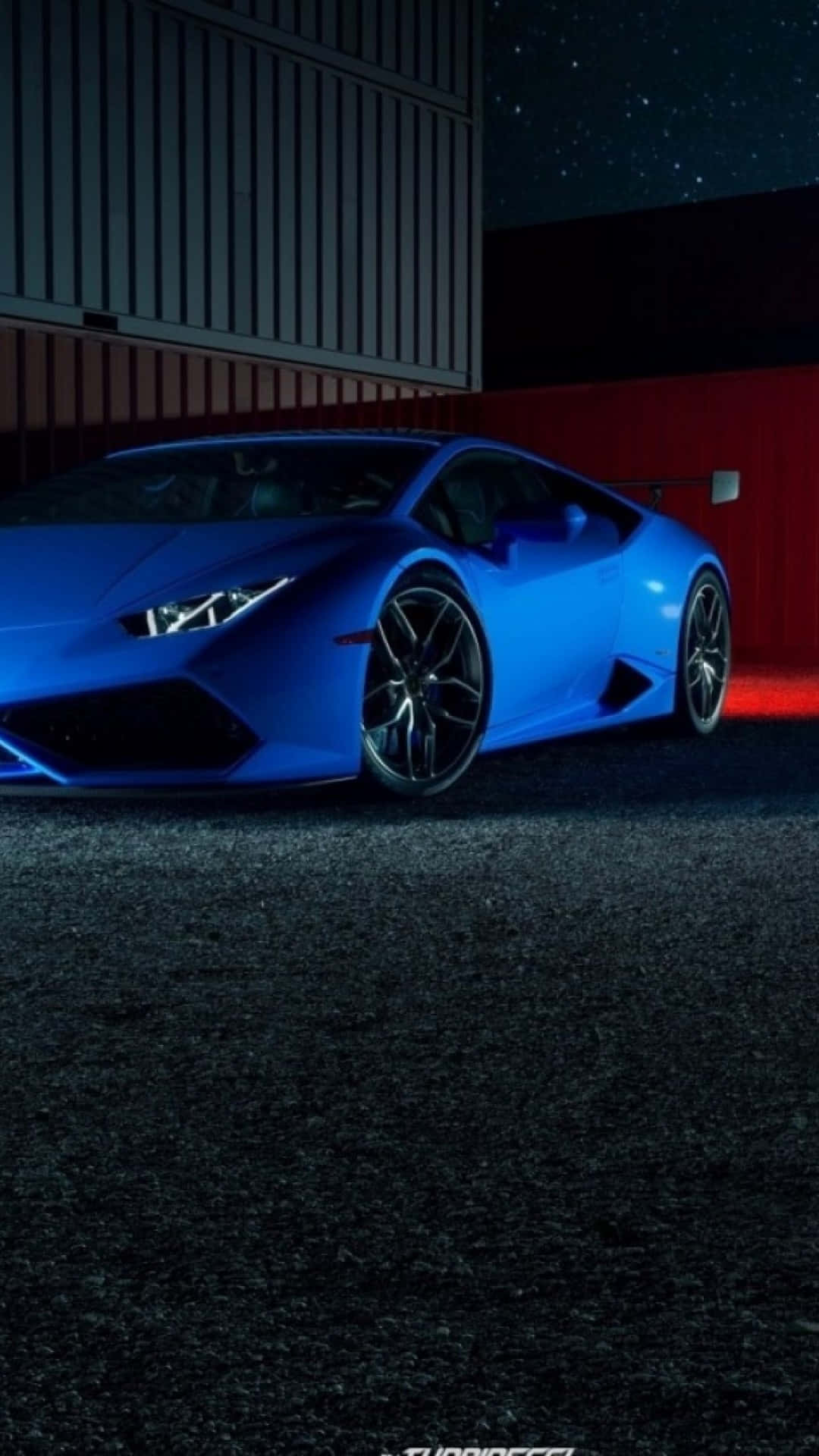 Blue Lamborghini iPhone 桌布 壁紙 — 一輛充滿活力的藍色藍寶堅尼Huracán跑車在星空下，旁邊是紅灰色的工業牆，閃閃發光。