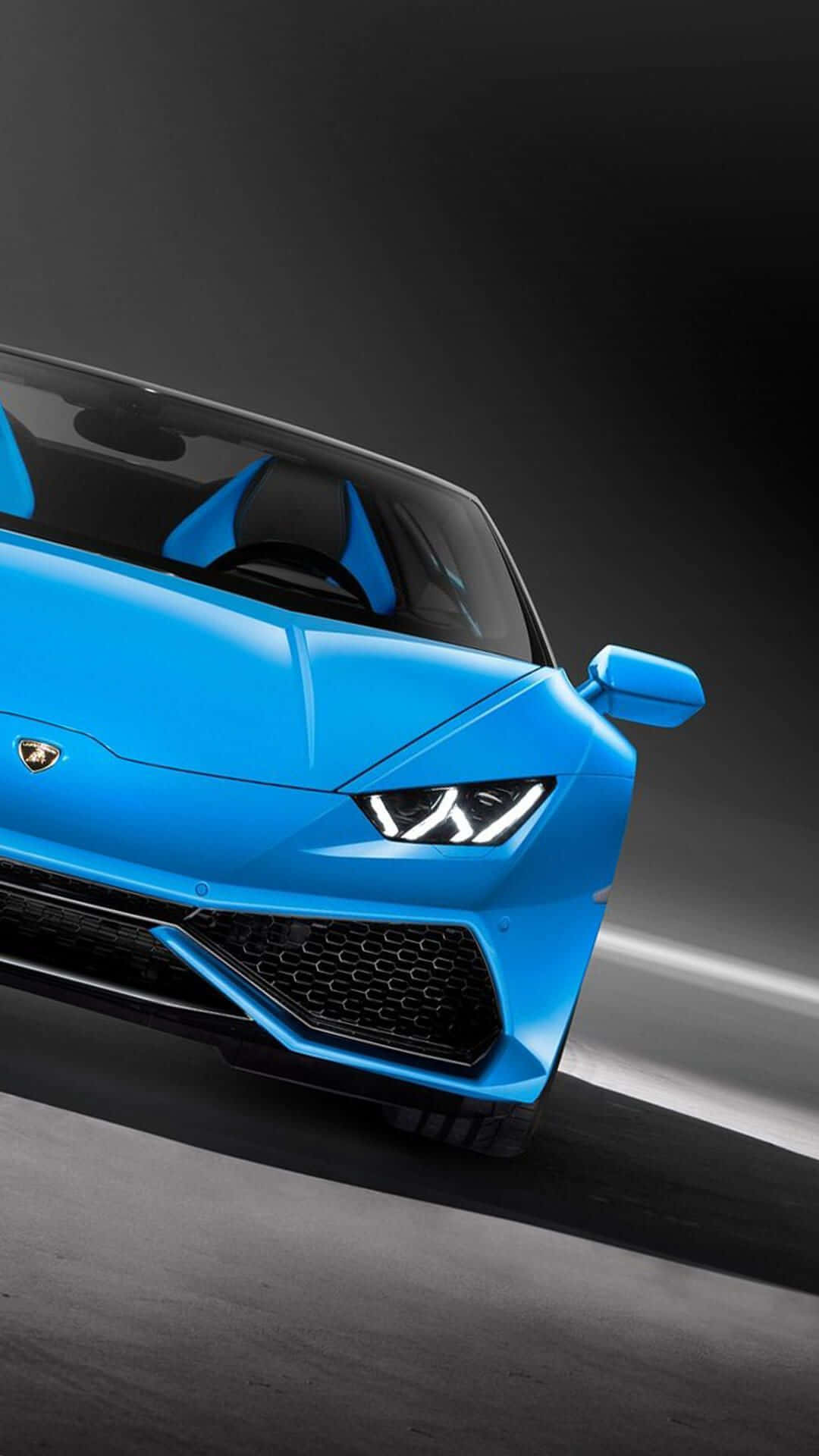 Blue Lamborghini iPhone 桌布 壁紙 — 一輛充滿活力的藍色藍寶堅尼跑車，車頭燈閃閃發光，在黑暗的攝影棚背景下形成銳利的角度。
